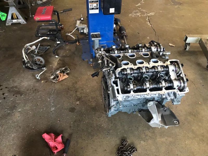 Engine partially disassembled on a garage floor with tools and parts scattered around.