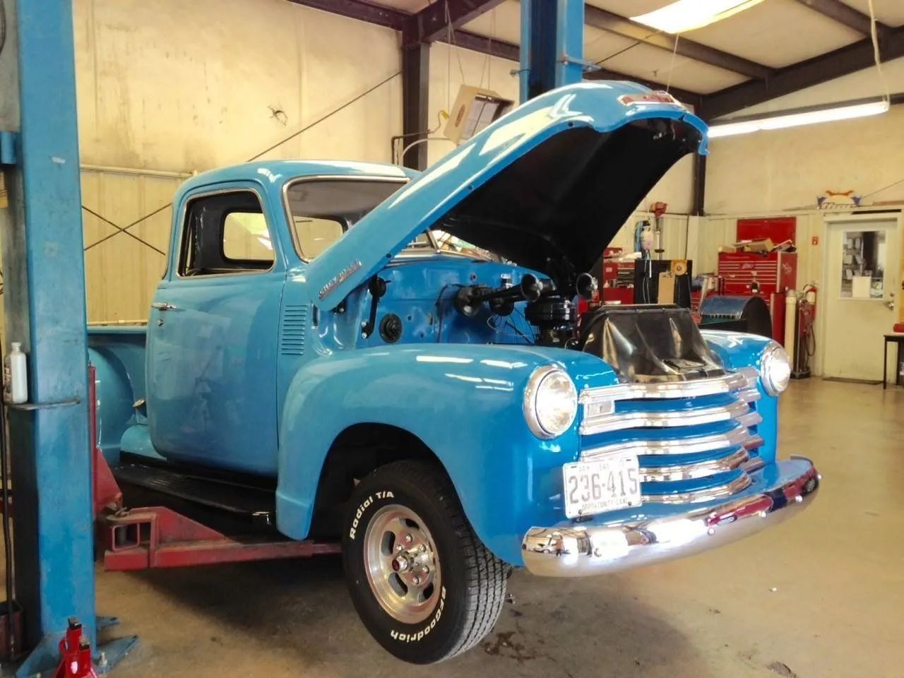 Blue vintage Chevrolet truck on a lift in a garage, hood open.