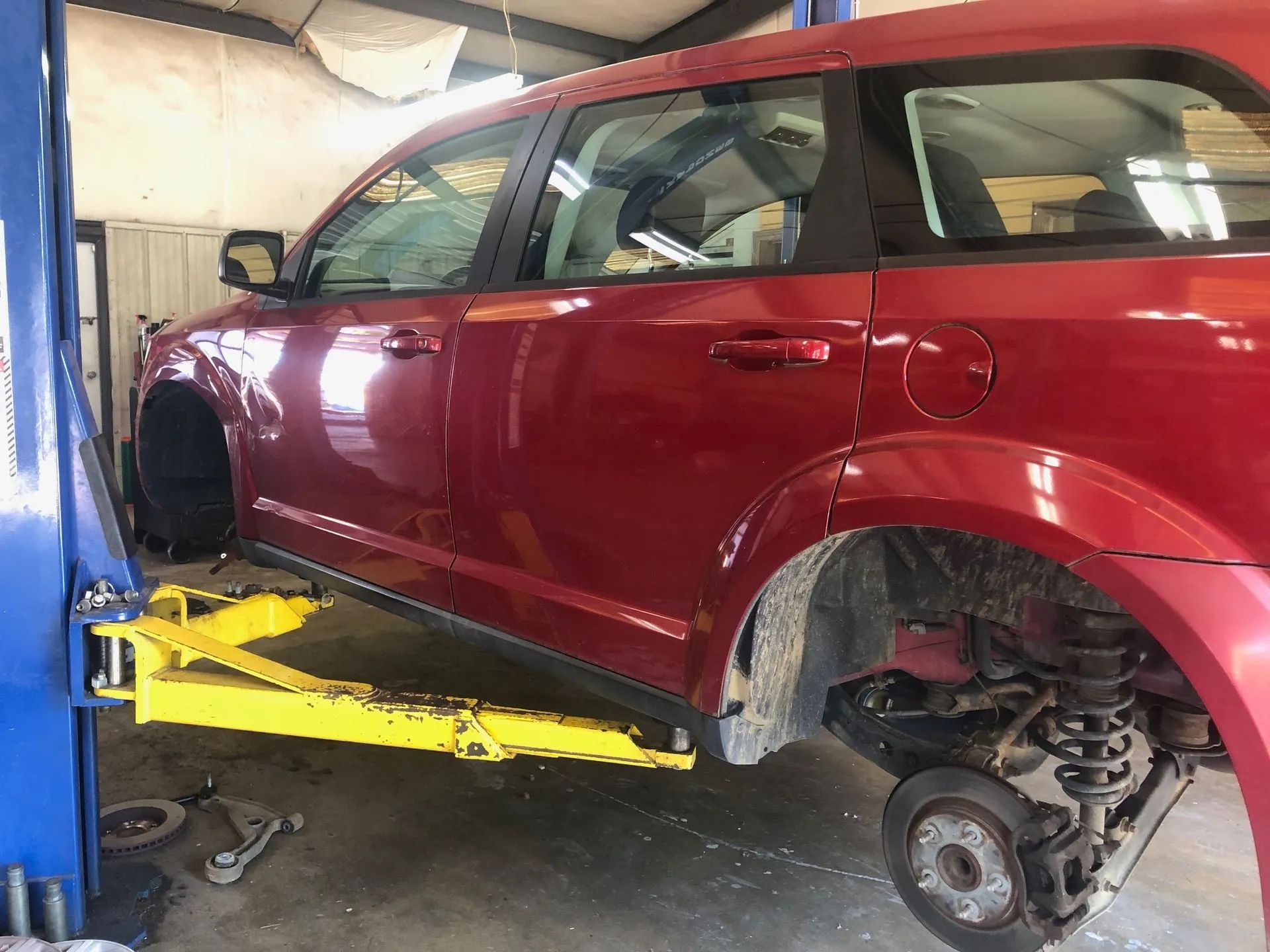 Red SUV on a yellow lift in a garage, wheels removed.