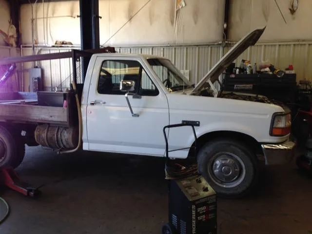 White pickup truck with a flatbed in a repair shop, hood open.