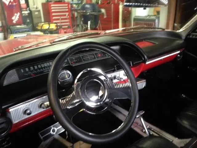 Classic car dashboard with red and black interior, chrome steering wheel and accents.