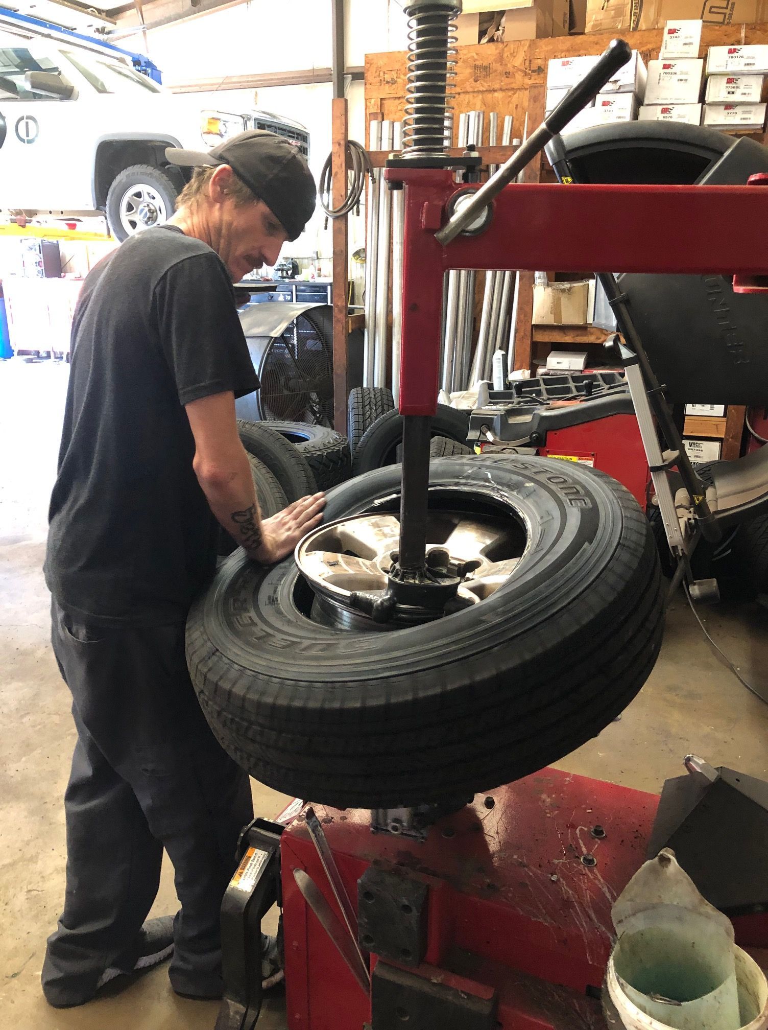 Mechanic changing a tire on a machine. Black shirt and hat, working inside a garage.