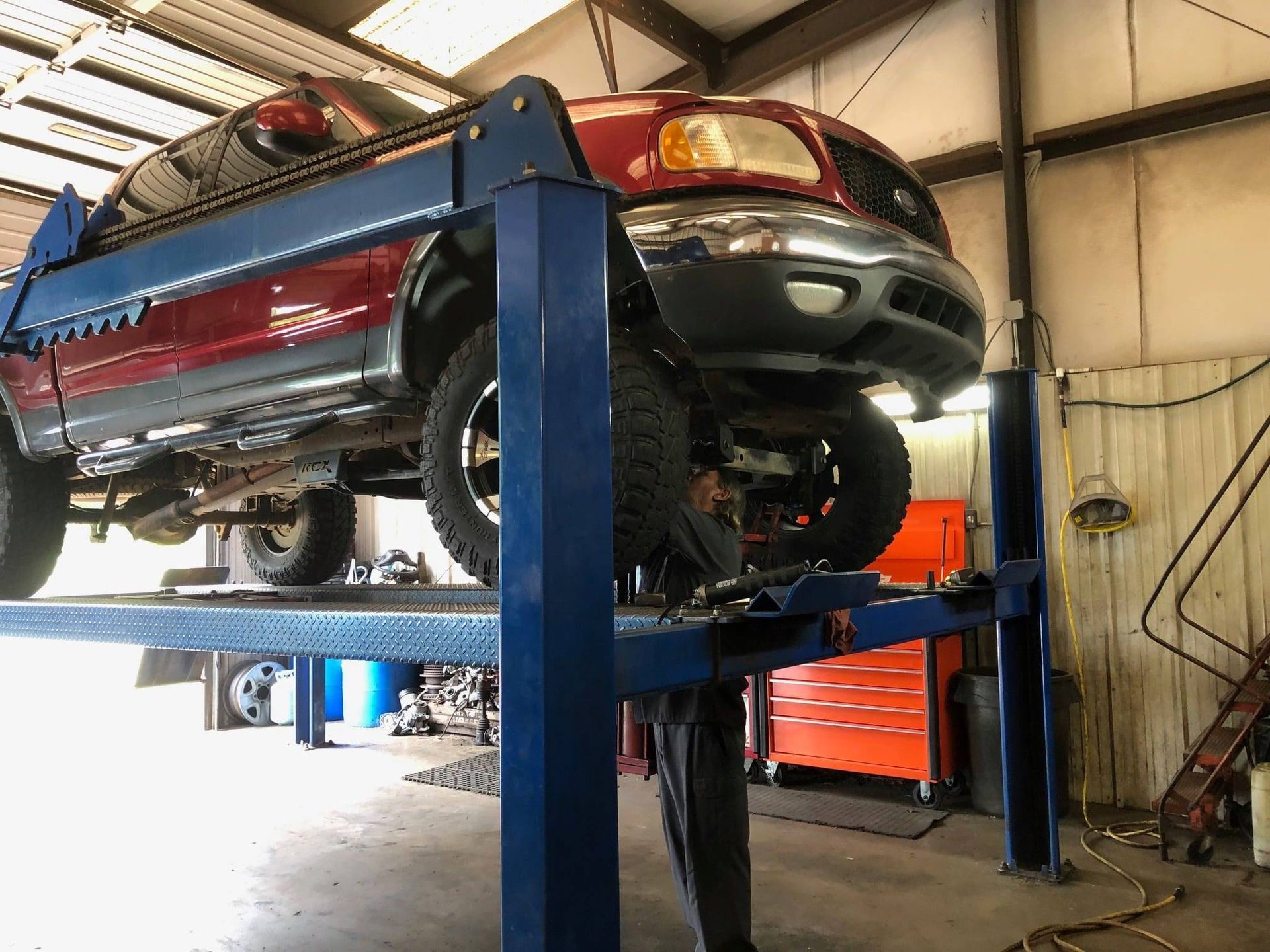 Red pickup truck on a blue auto lift inside a repair shop.