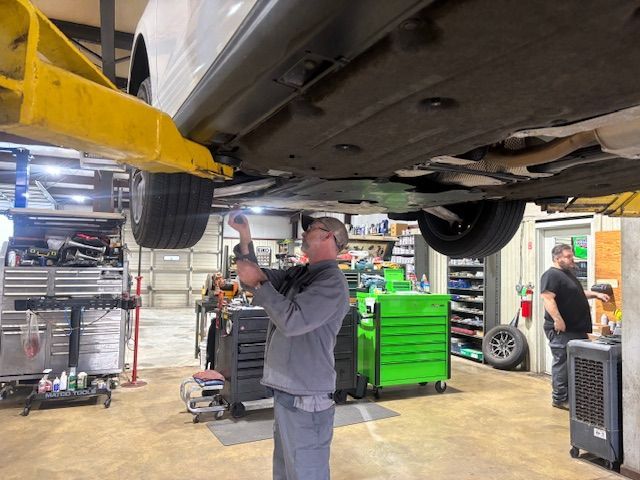 A mechanic working on a car raised on a lift in a garage, using a tool.