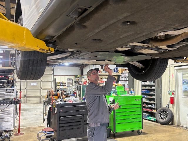 Mechanic inspecting the undercarriage of a car raised on a lift in a shop.