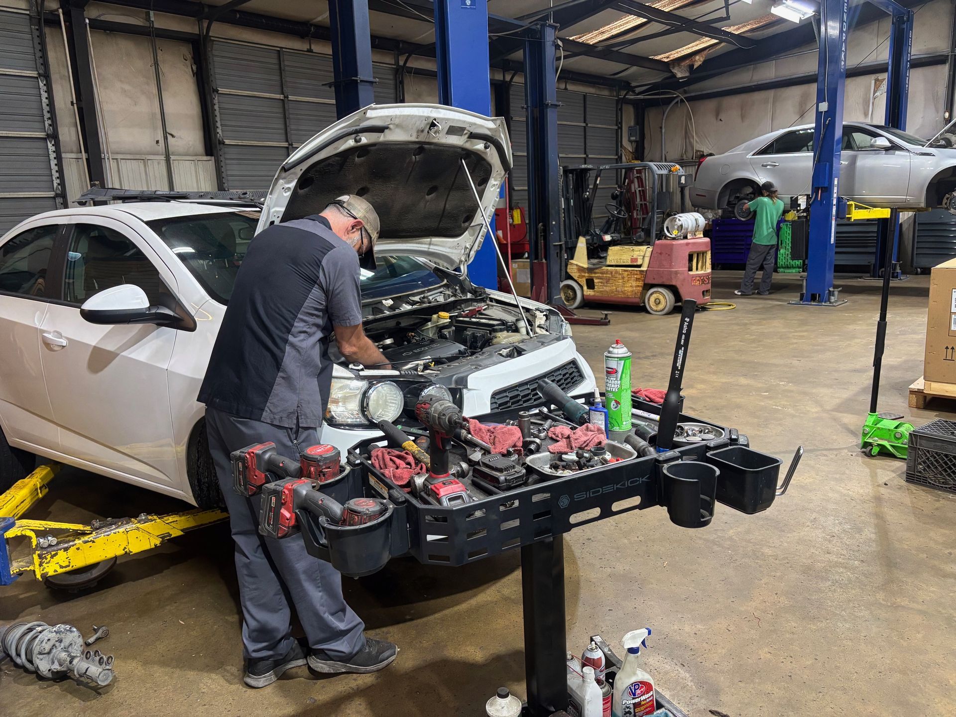 Mechanic working on a white car in a garage with the hood open and tools on a workbench