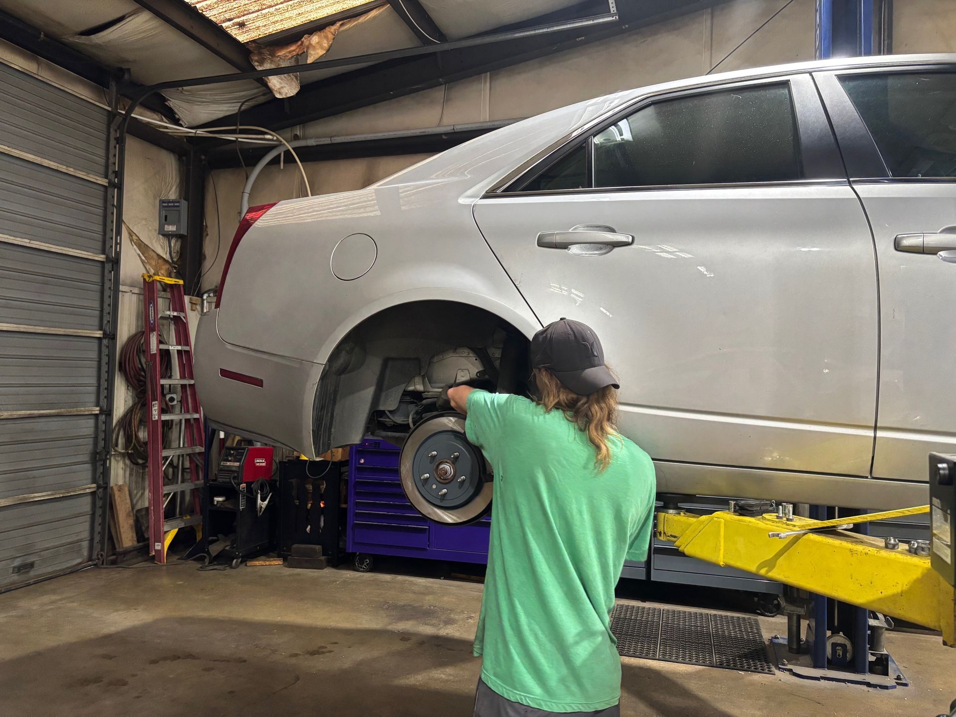 Mechanic working on a silver sedan raised on a lift in a garage