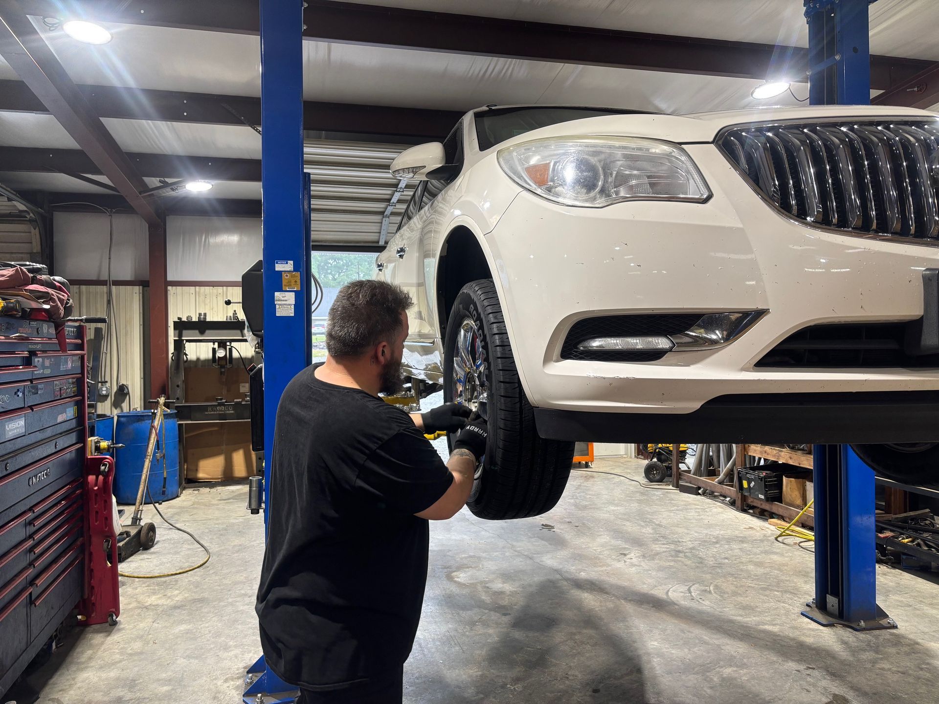 Mechanic inspecting a white SUV on a lift in an auto repair shop