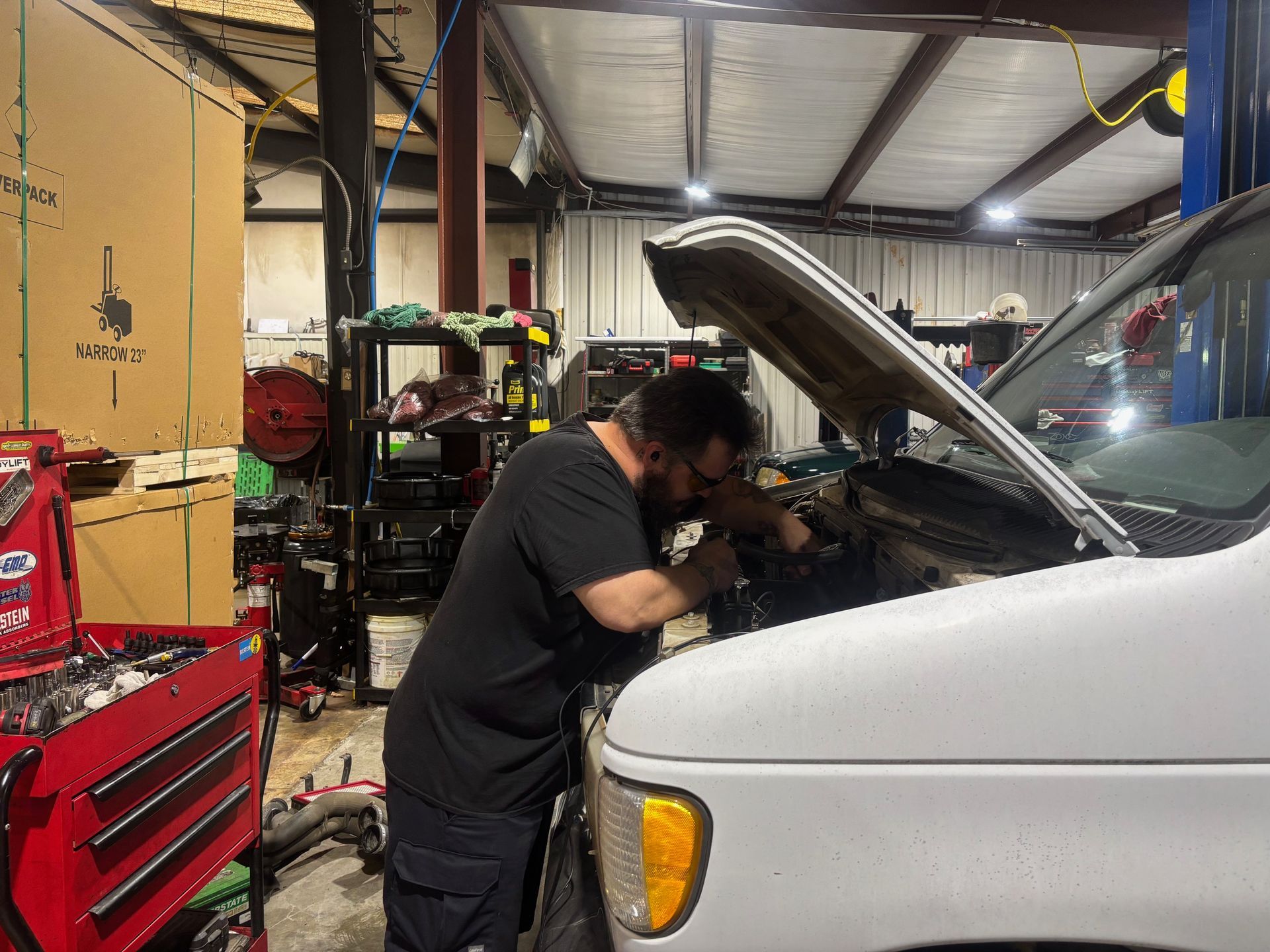 Mechanic working under open hood of a white van in an auto repair shop