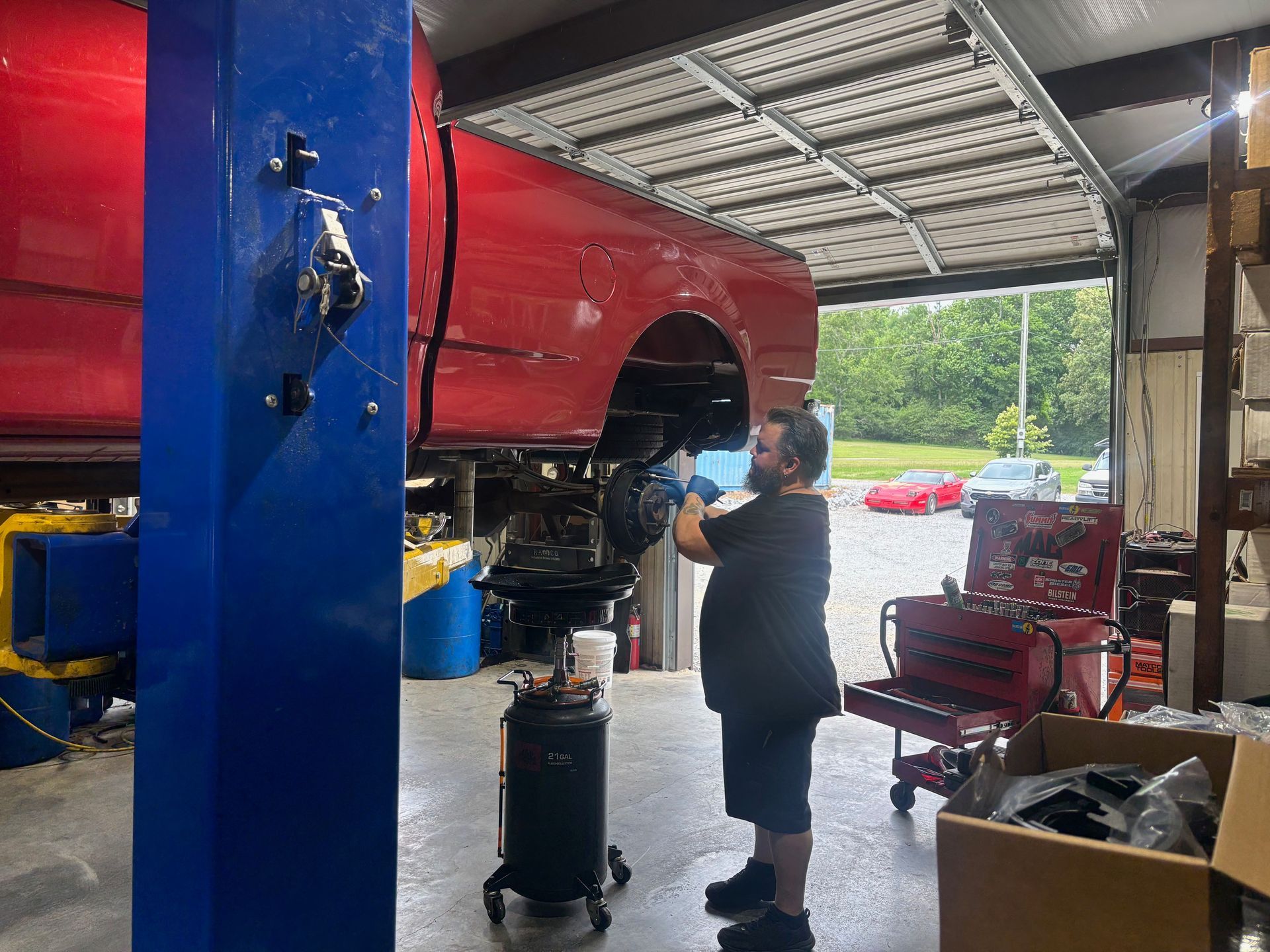 Mechanic working under a red pickup truck raised on a lift inside an auto shop