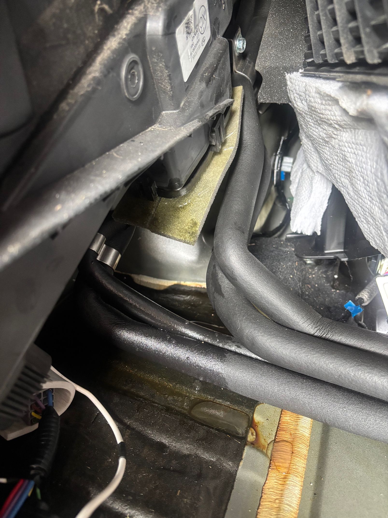 Close-up of car engine compartment with hoses, wiring, and a yellow-green fluid leak stain.