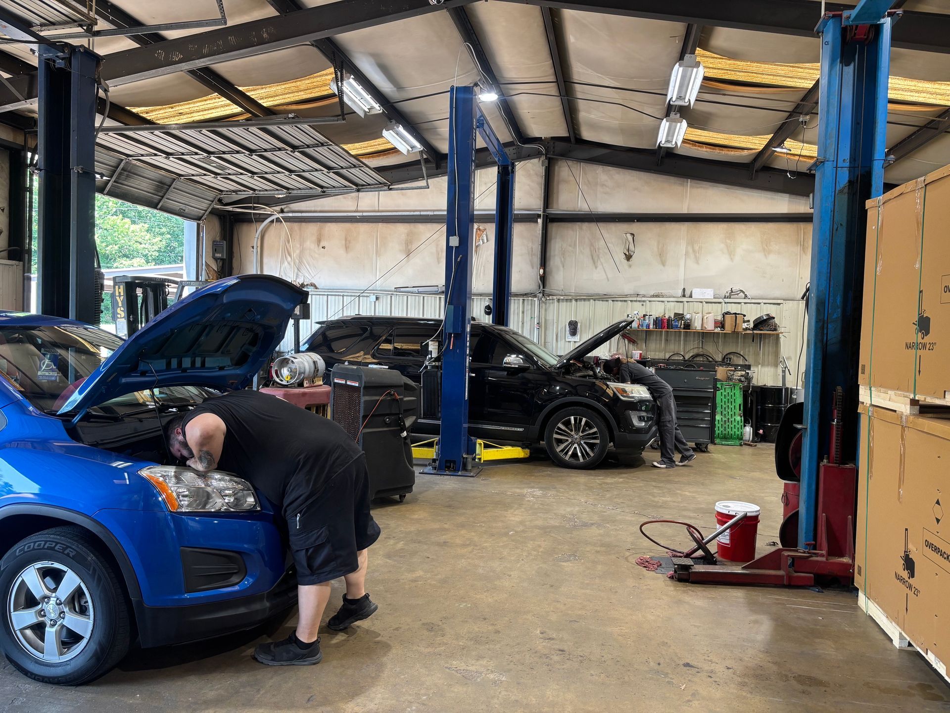 Mechanic working on a blue car in an auto repair garage with open hood and tools nearby