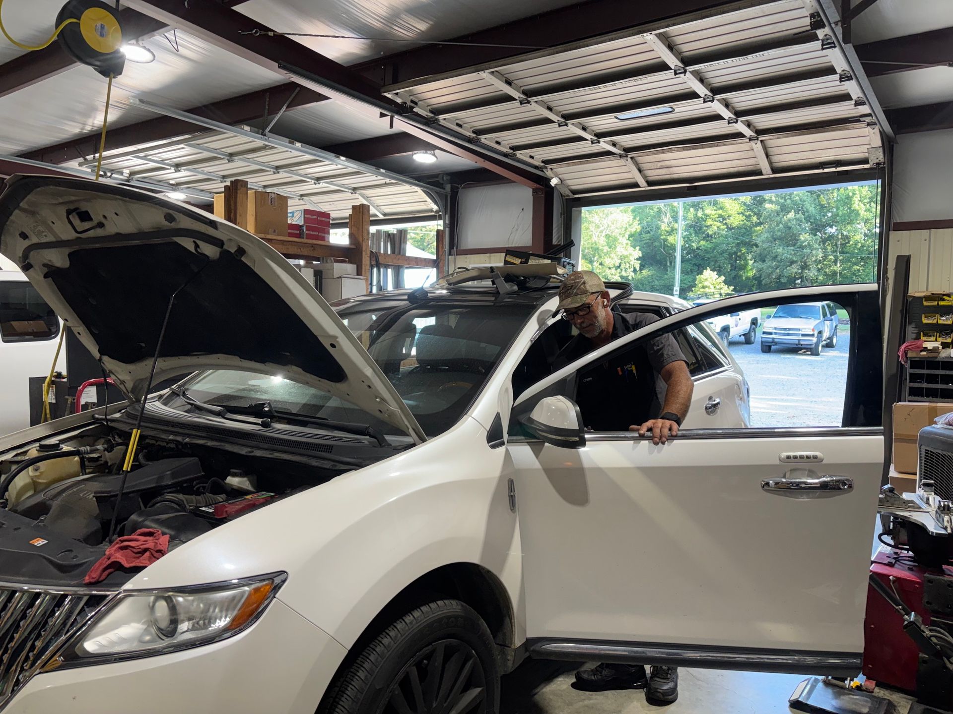 White SUV in a garage with hood open, and a person leaning out of the driver’s door.