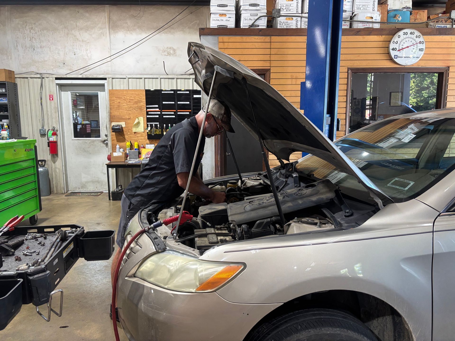 Mechanic working under the hood of a silver car in an auto shop garage
