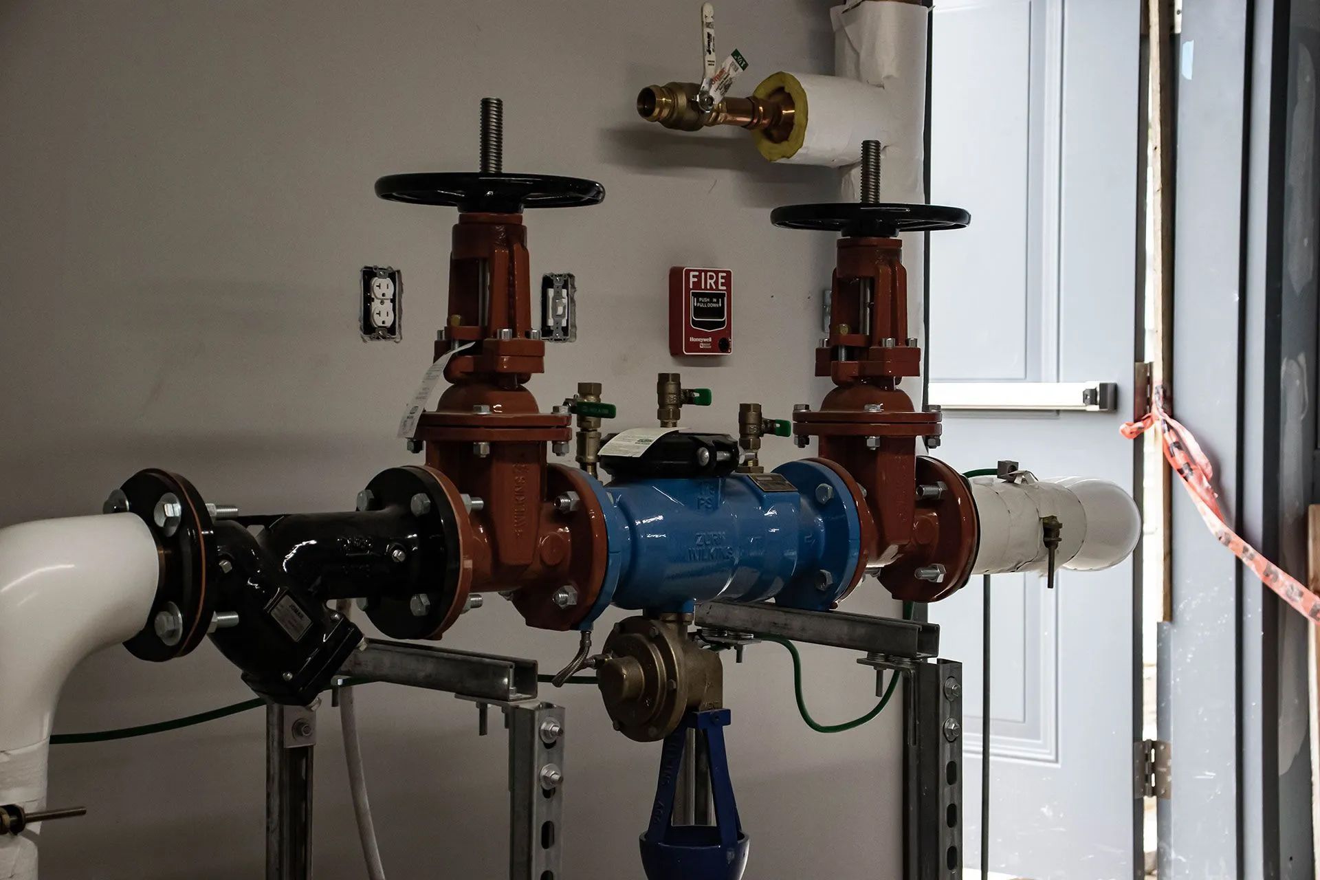 Plumbing system with red and black valves, a blue water meter, and white and black pipes.