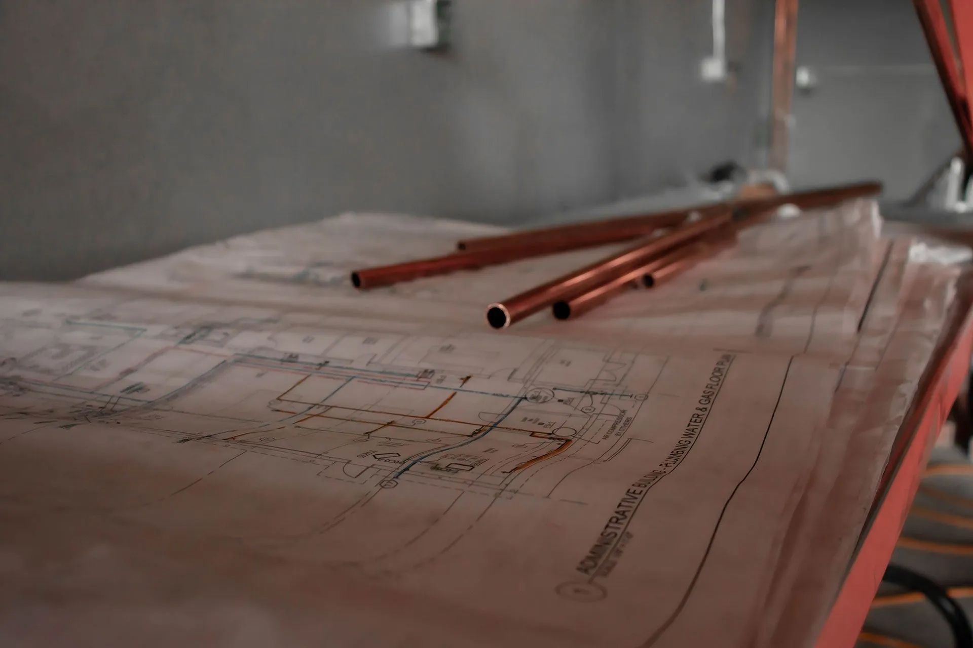 Blueprints with copper pipes on a work surface, possibly for plumbing in a construction setting.