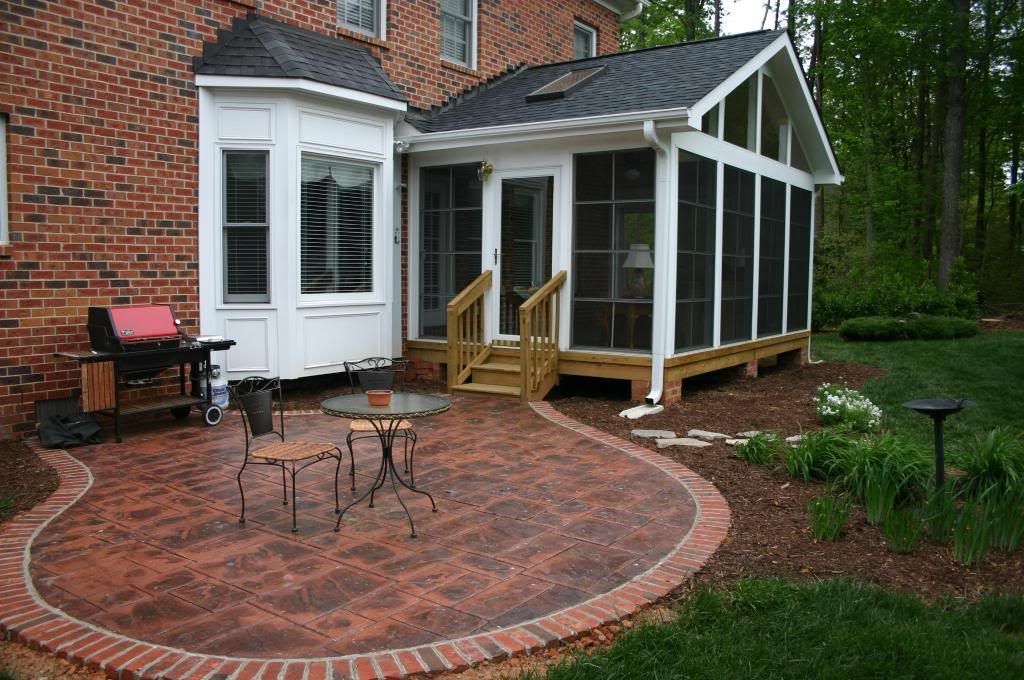 A screened in porch in the backyard of a brick house