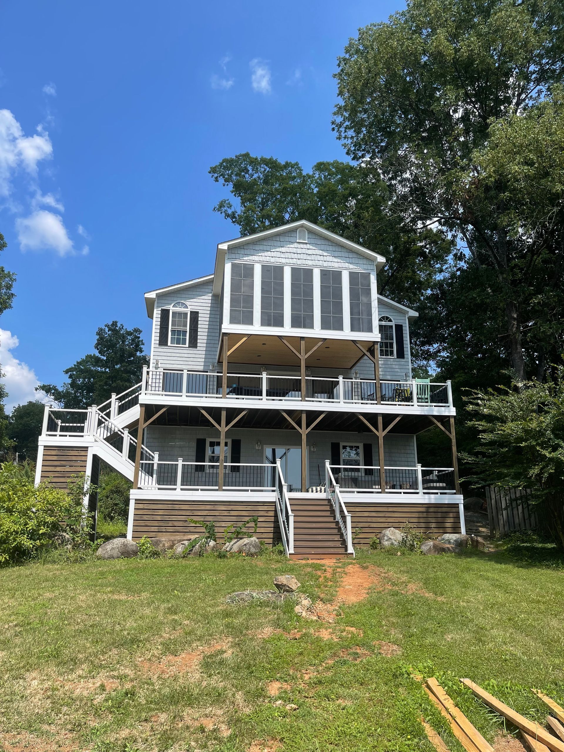 A large white house with a large deck is sitting on top of a grassy hill.