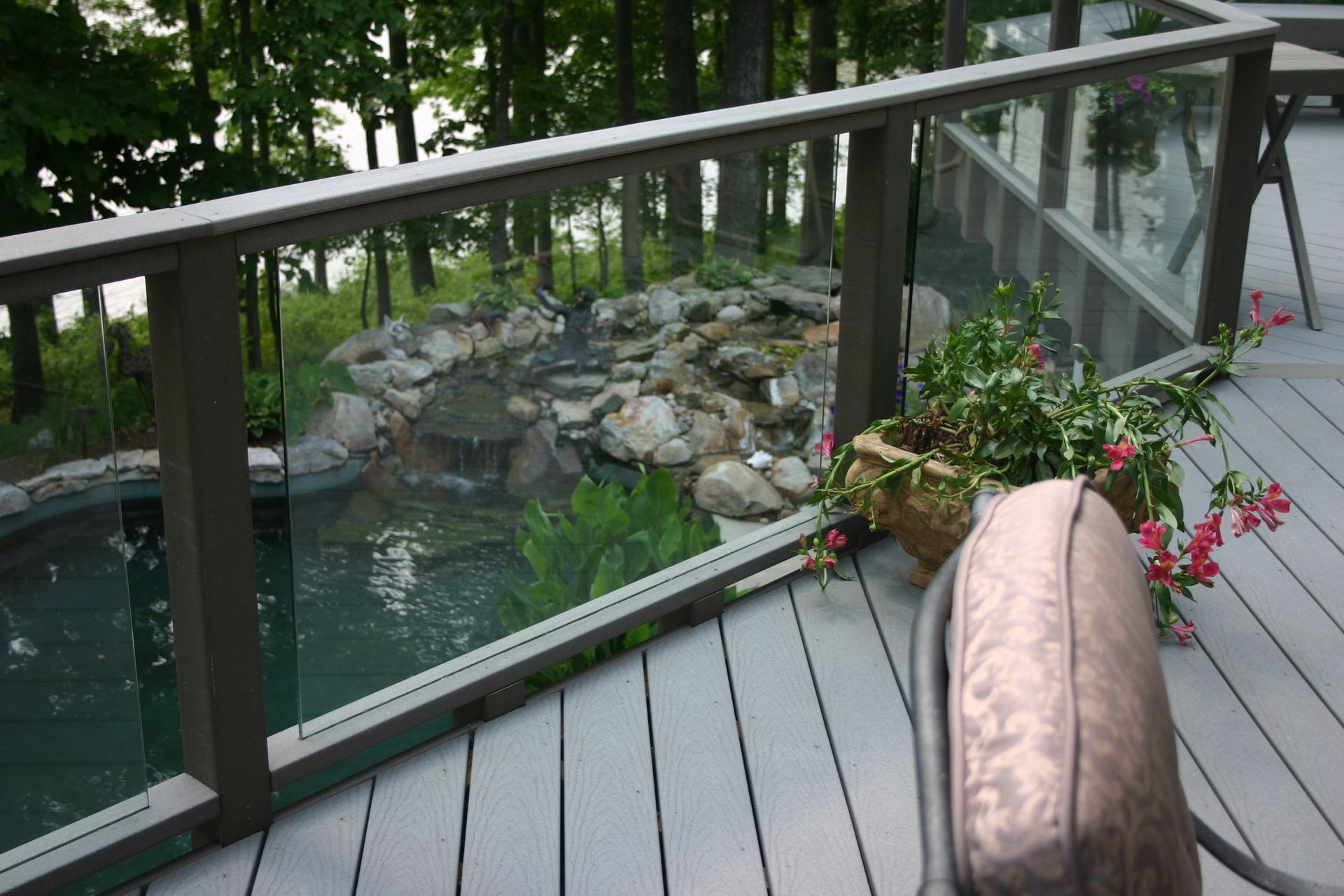 A deck with a glass railing overlooking a pond