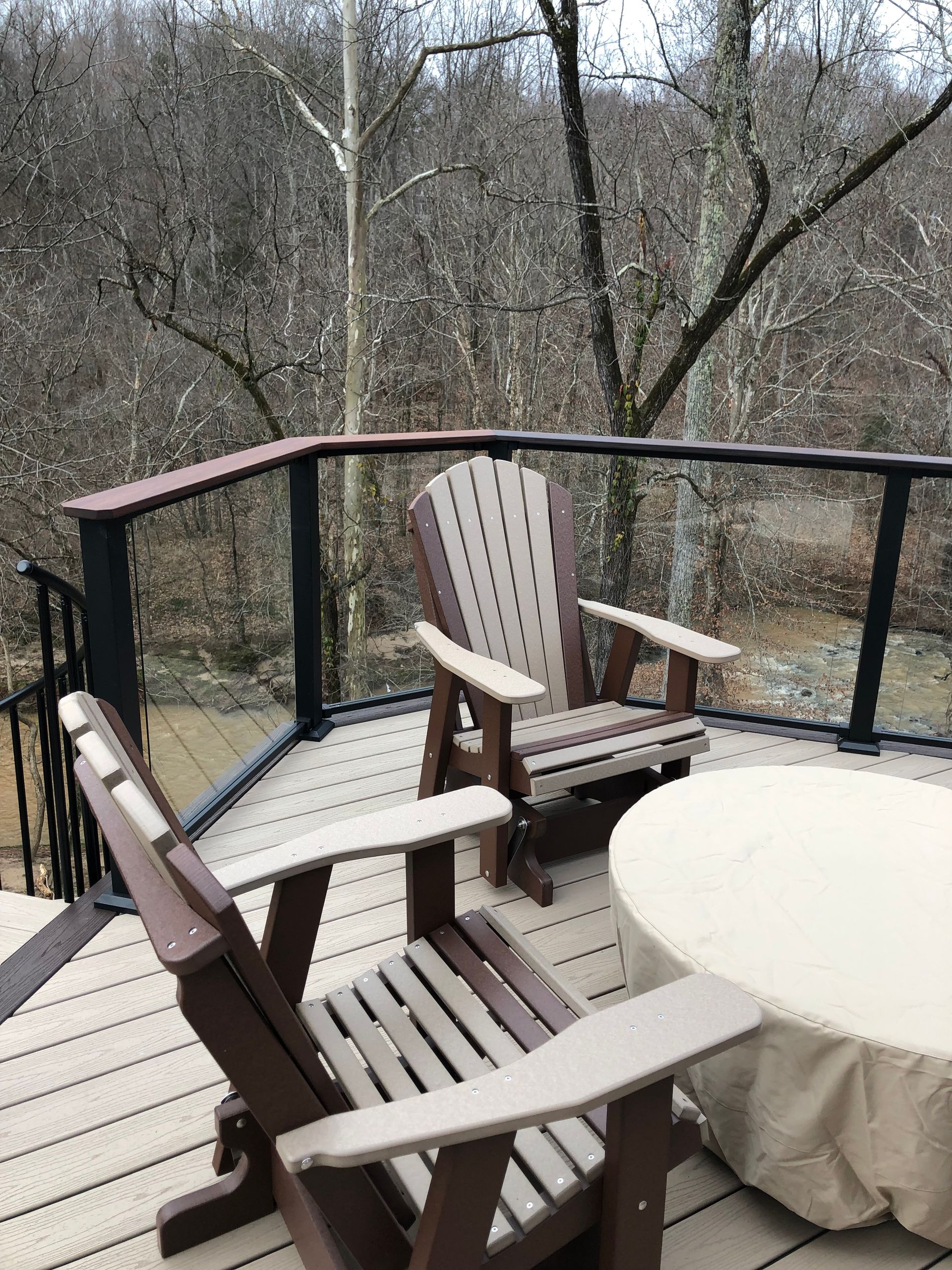 Two chairs and a table on a deck with trees in the background.