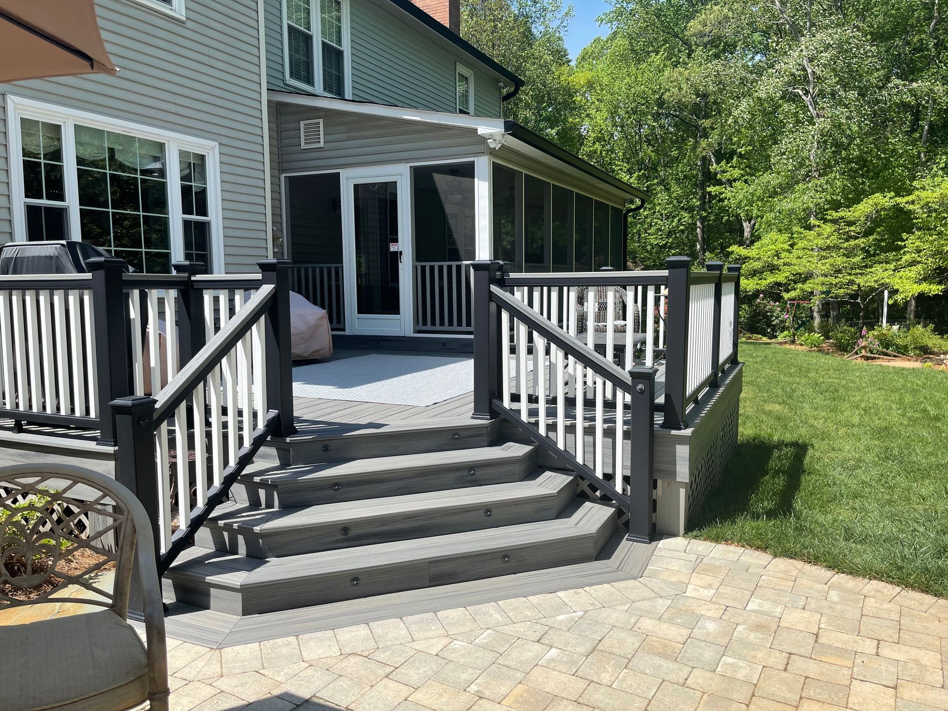 A deck with stairs leading to a screened in porch and a house in the background.