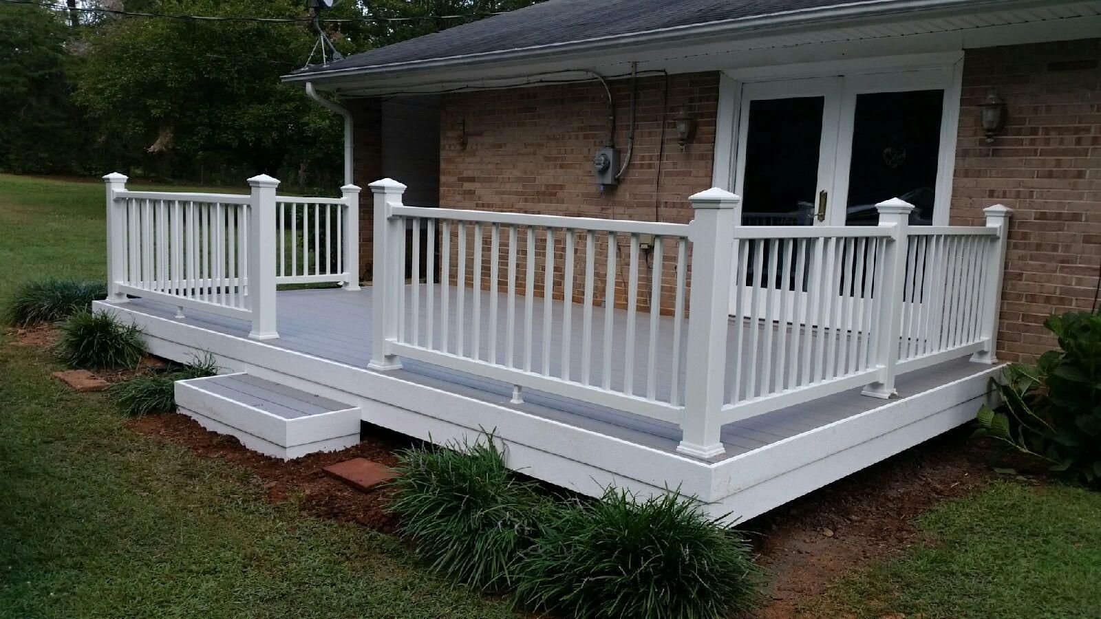A white deck with a white railing is in front of a brick house.