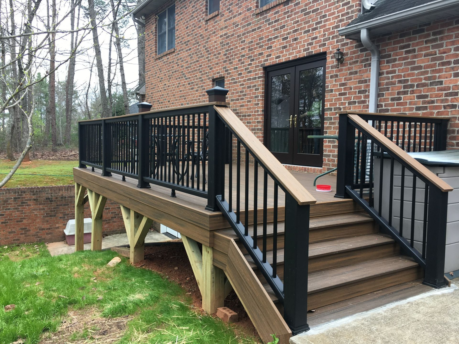A wooden deck with black railing and stairs in front of a brick house.