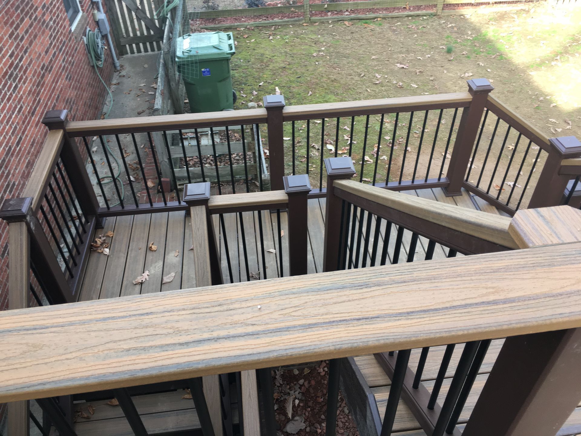 A wooden deck with stairs leading up to it and a trash can in the background.