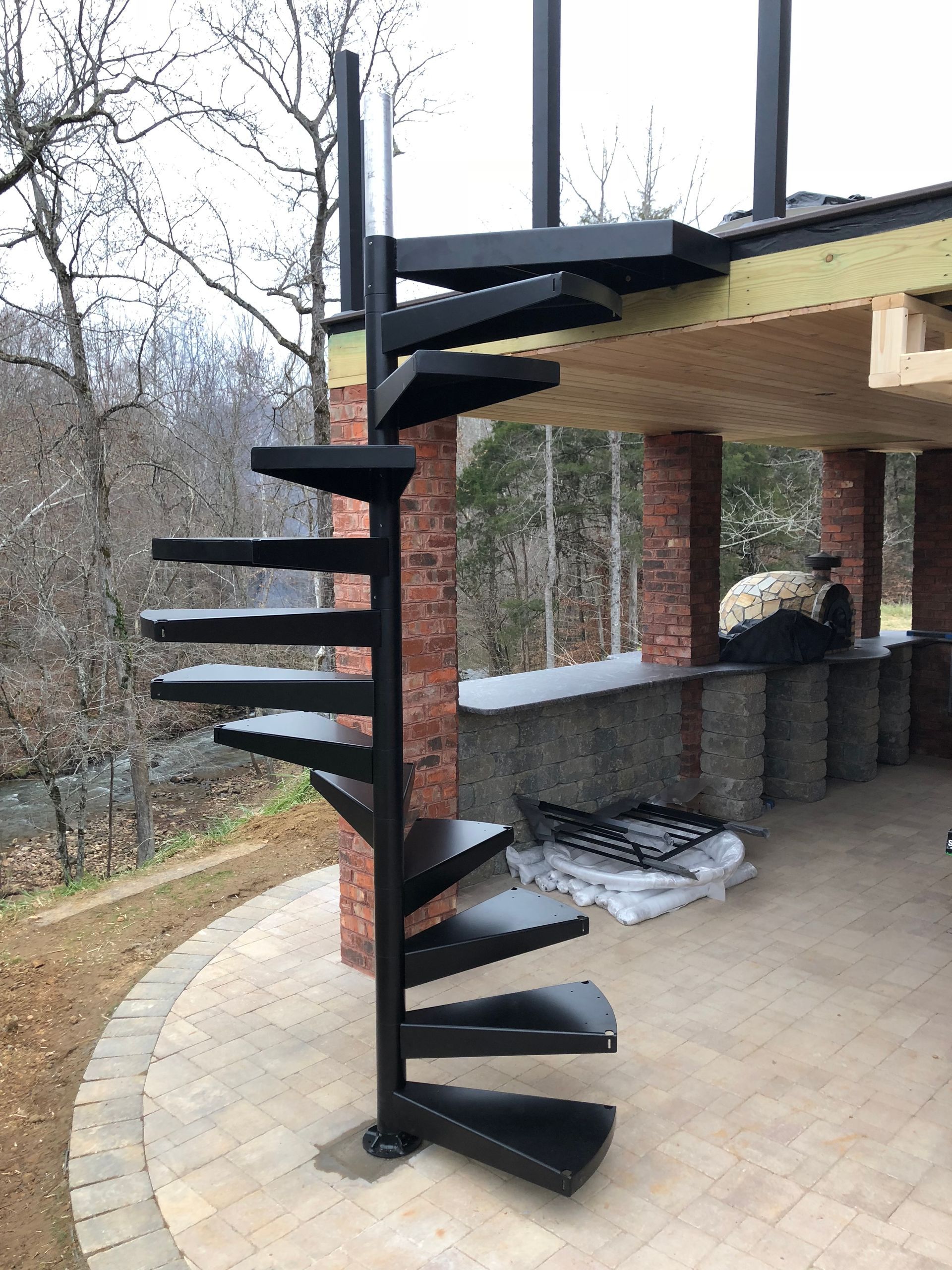 A spiral staircase is sitting on top of a patio next to a brick wall.