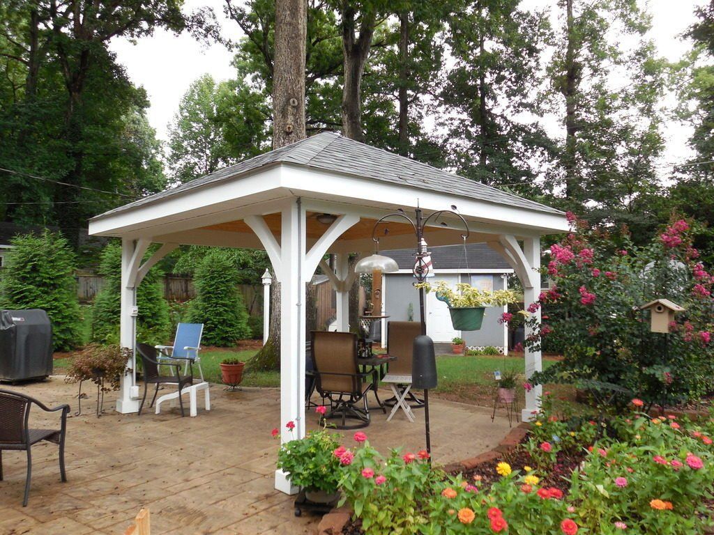 There is a gazebo in the middle of a garden with chairs and flowers.