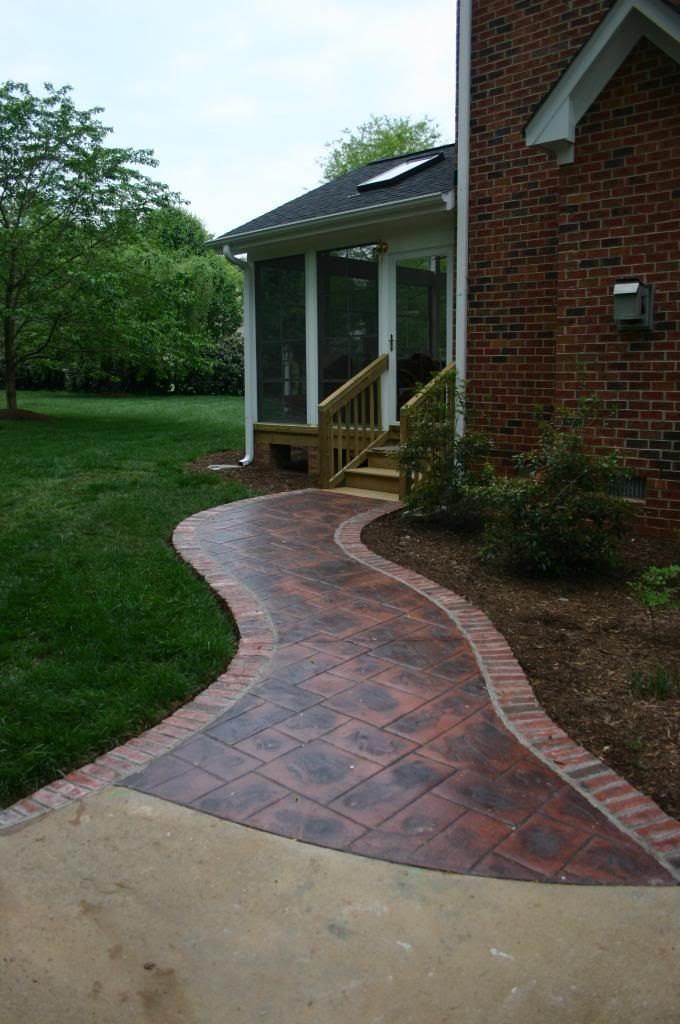 A brick walkway leading to a screened in porch of a brick house.