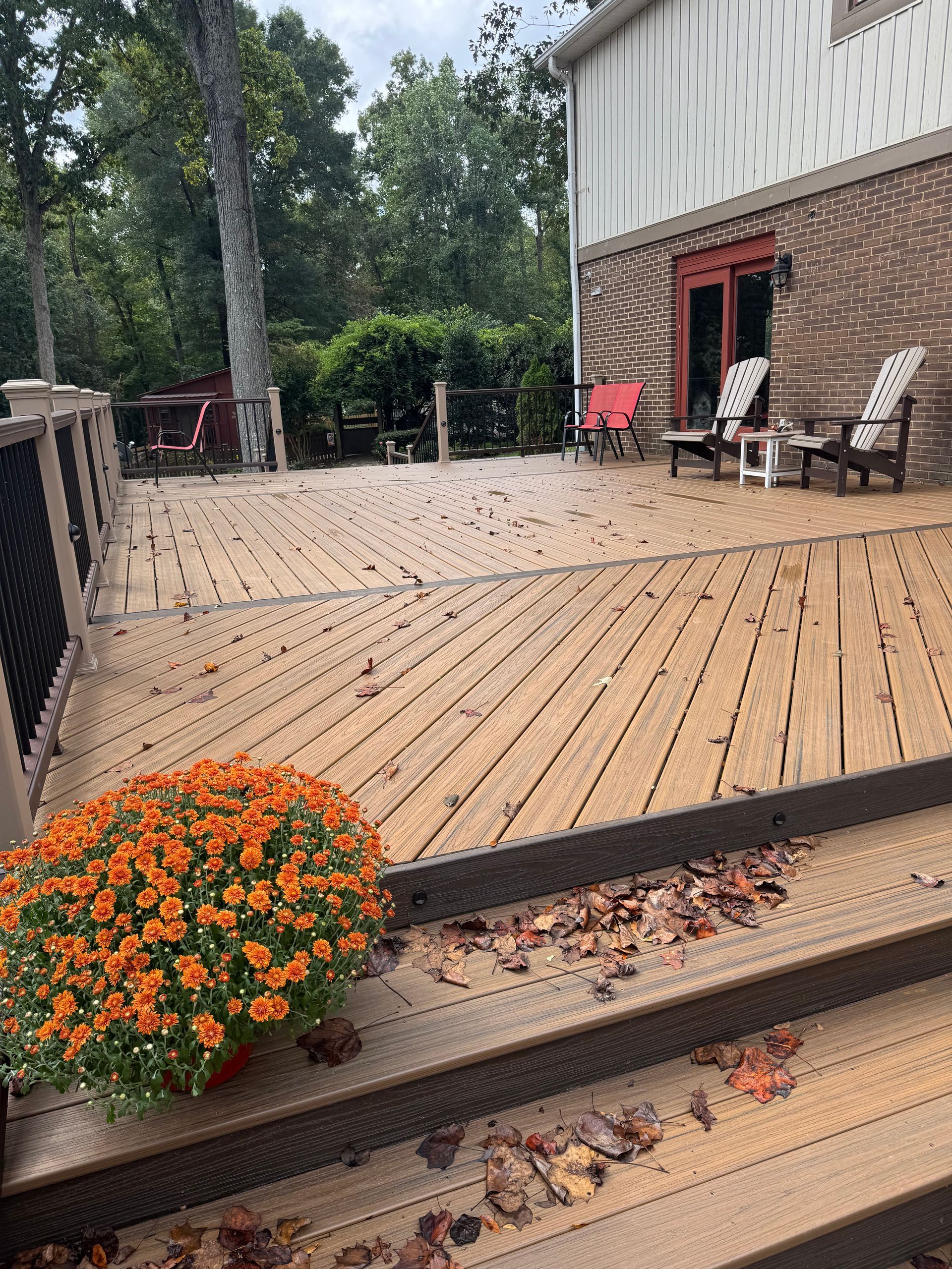 Wooden deck with orange flower pot, fallen leaves, and brick house exterior.