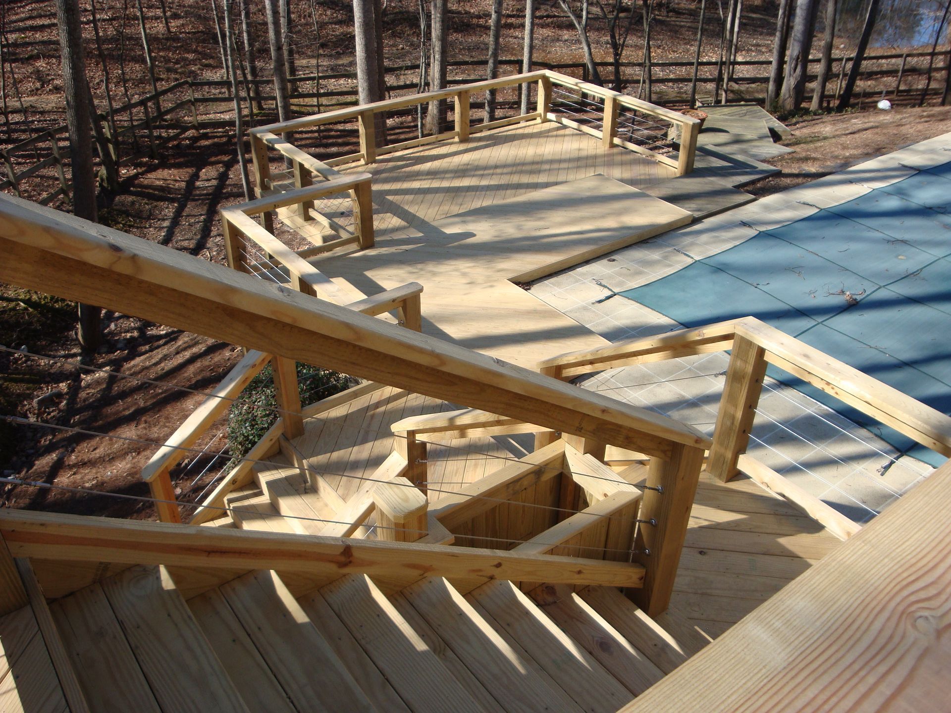 Wooden deck with stairs leading to a pool covered in blue tarp, surrounded by trees.