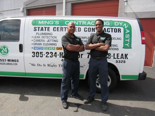 Two men in work uniforms stand by a van with 