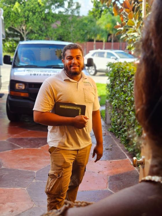 Man in tan work clothes at a doorway holding a clipboard, with a company van parked behind him.