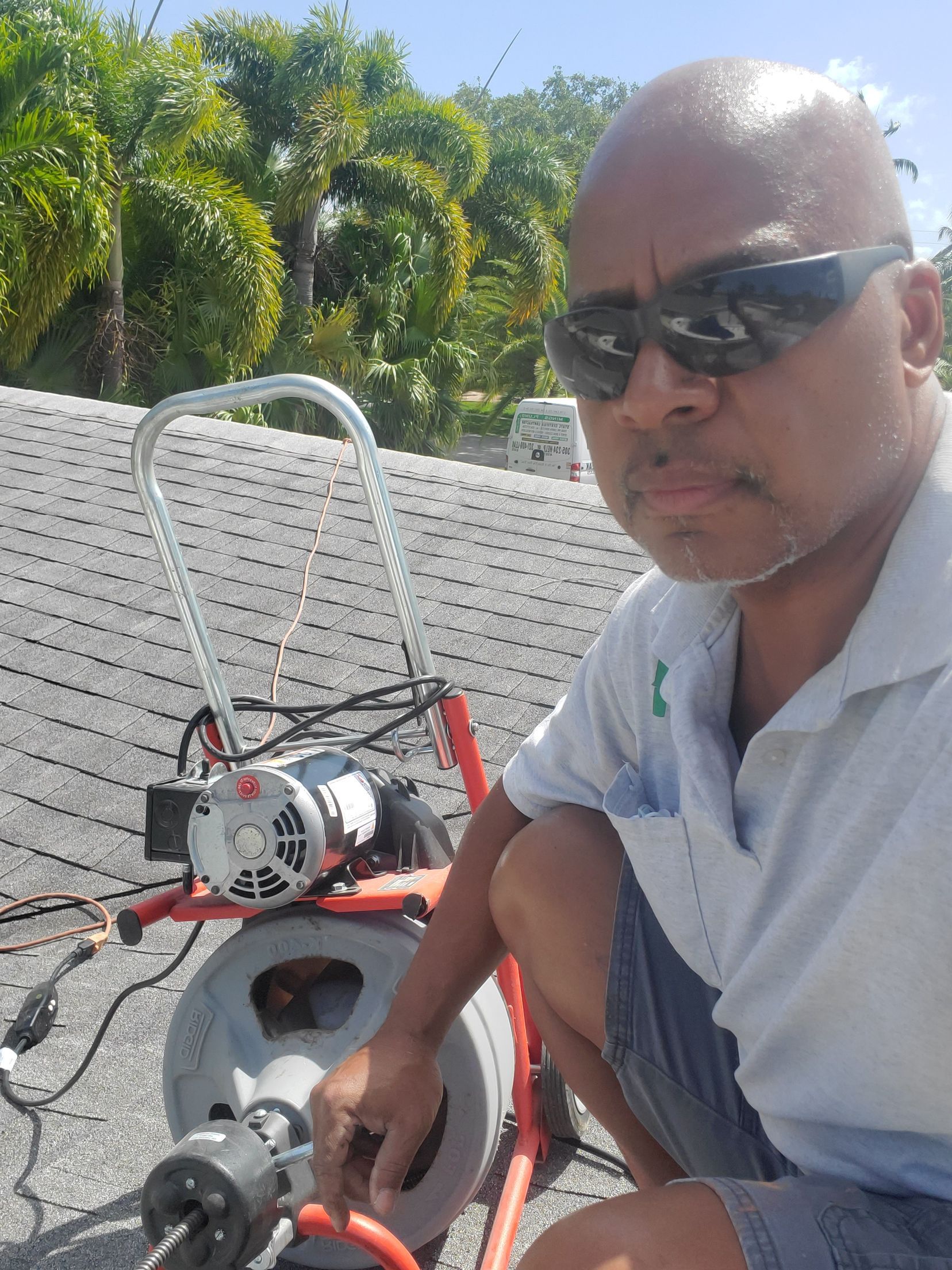 Man in sunglasses and light-colored shirt operates a drain cleaning machine on a rooftop.