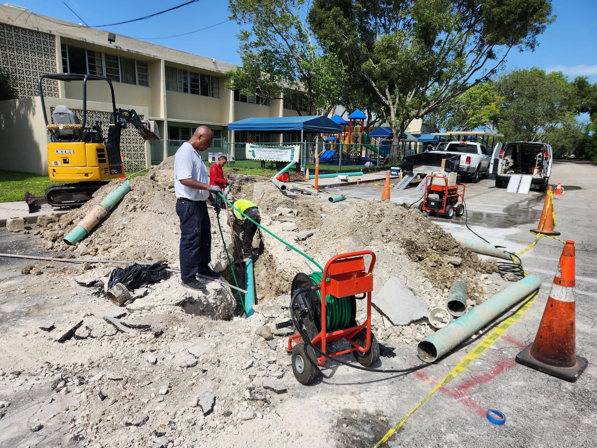 Construction worker operating equipment on a pile of dirt, near pipes and a small excavator.
