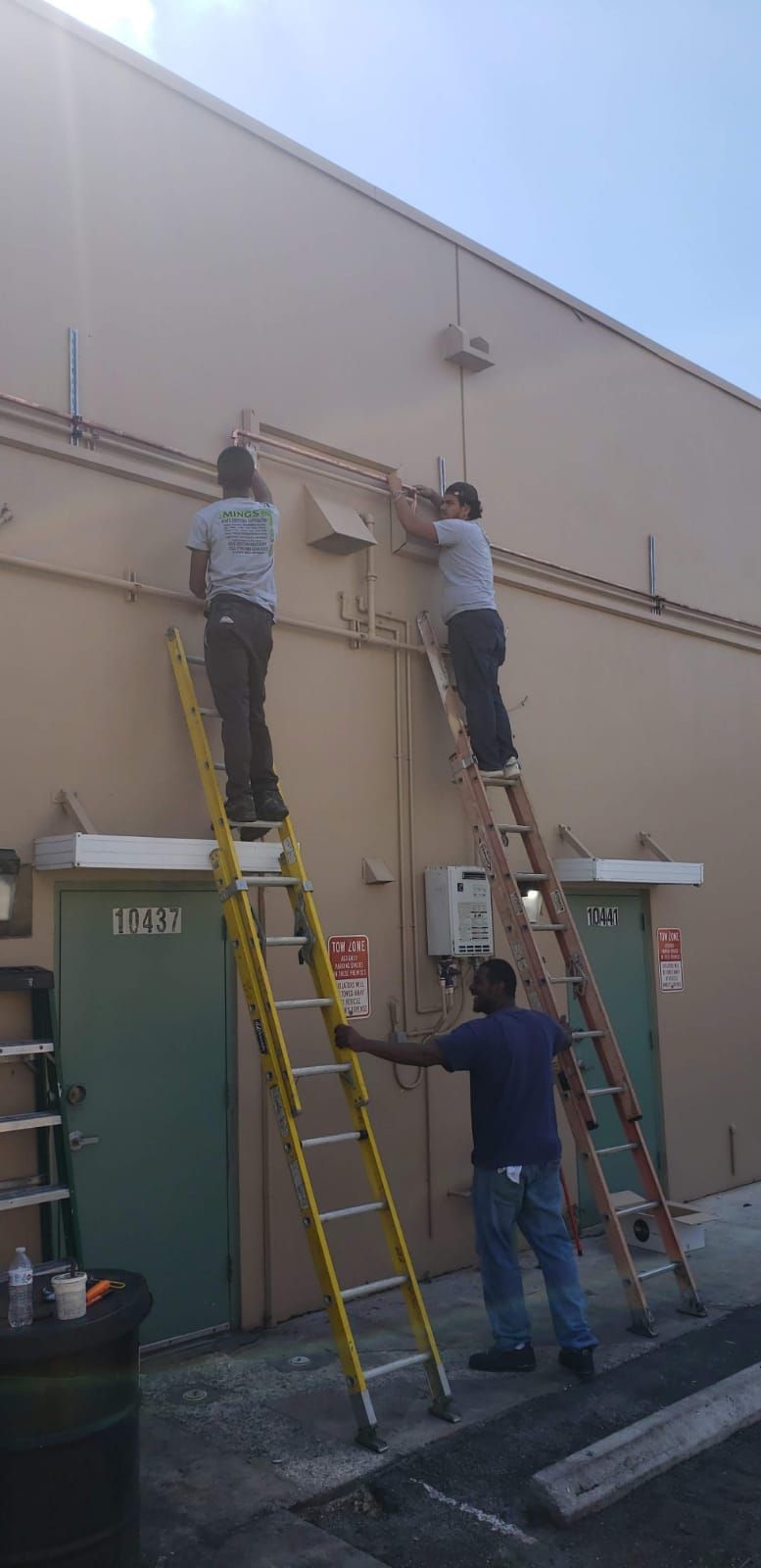 Three workers on ladders, installing wiring on a building's exterior.