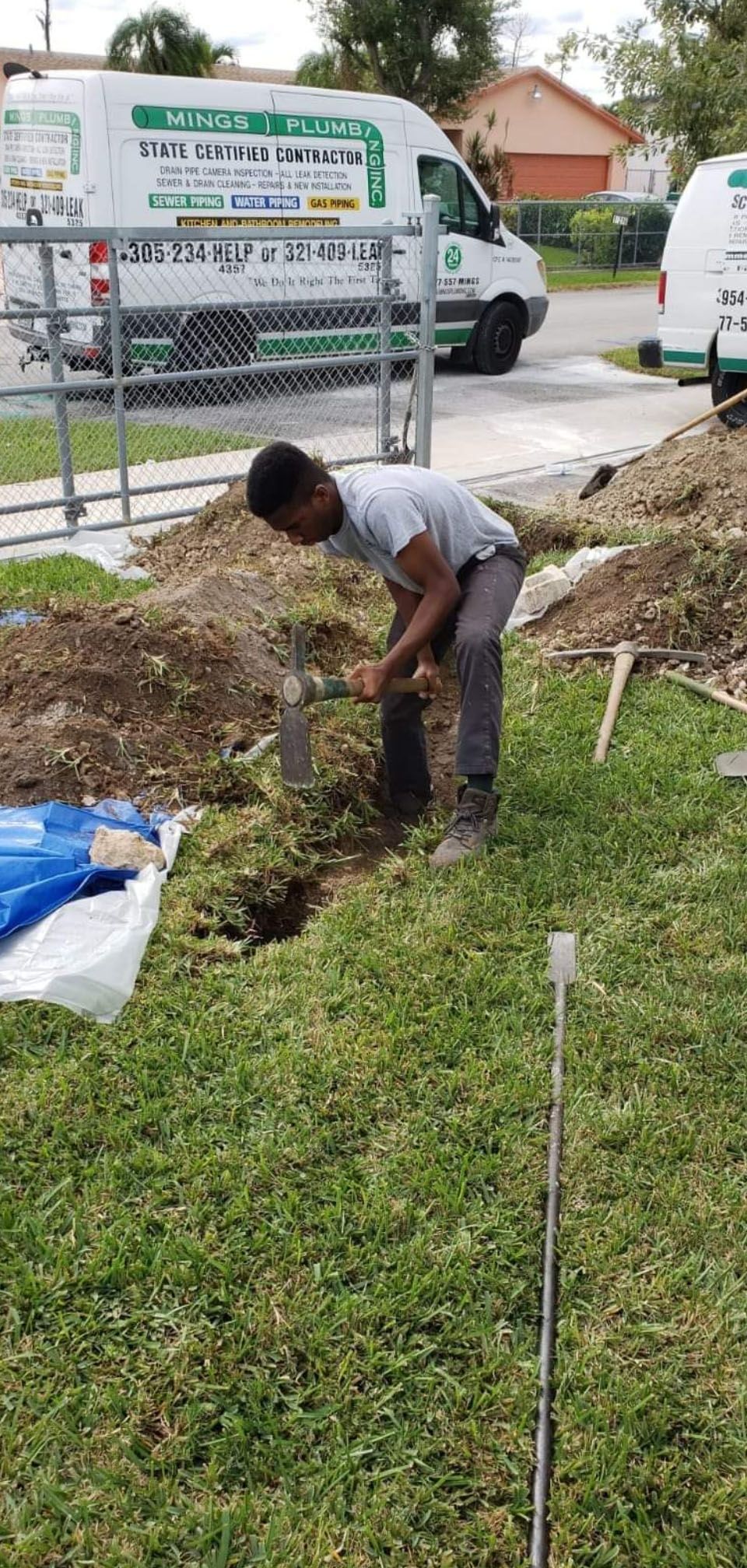 Person digging in the grass with a shovel, two white vans in the background.