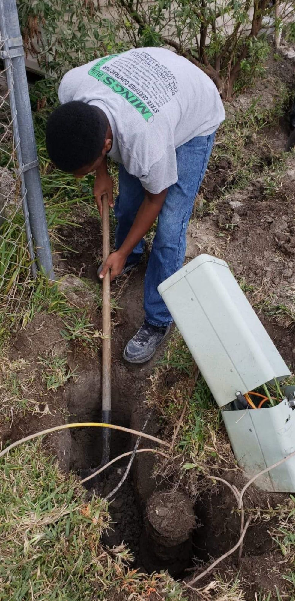 Person using a shovel to dig in the ground near a utility box.