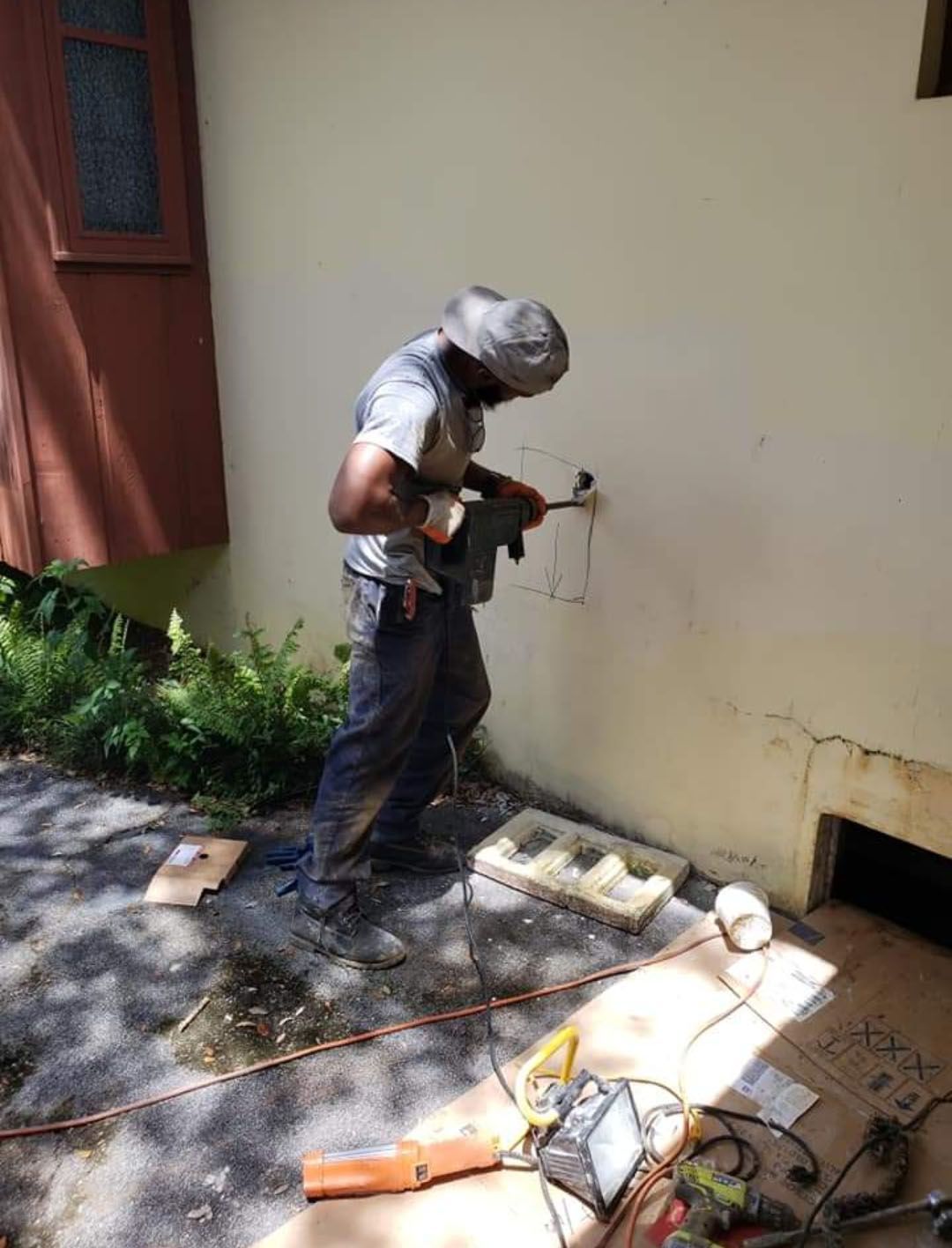 Person using a tool to cut a circle in a light yellow wall outdoors.