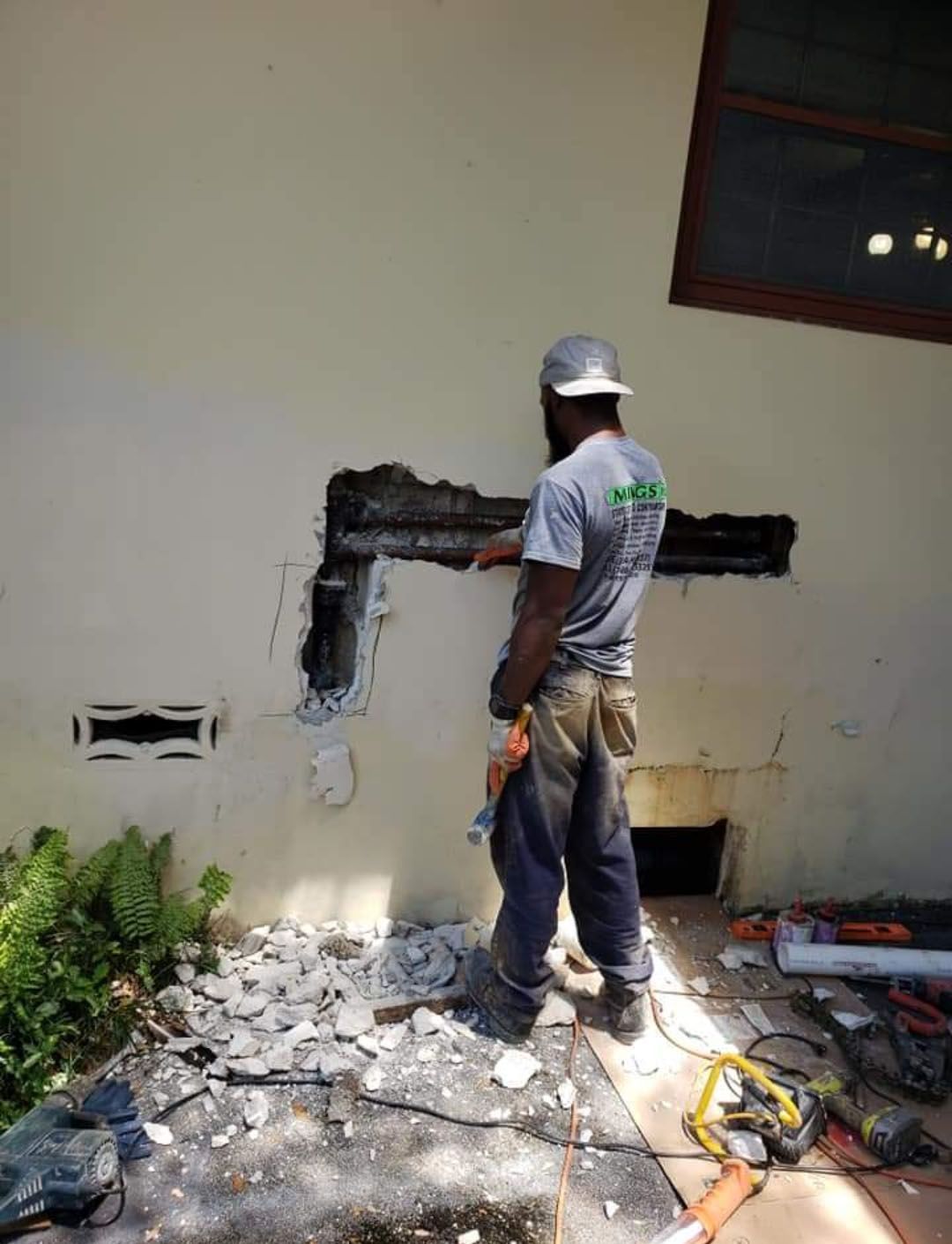 Construction worker repairing a wall, removing debris. Outdoors, sunny.