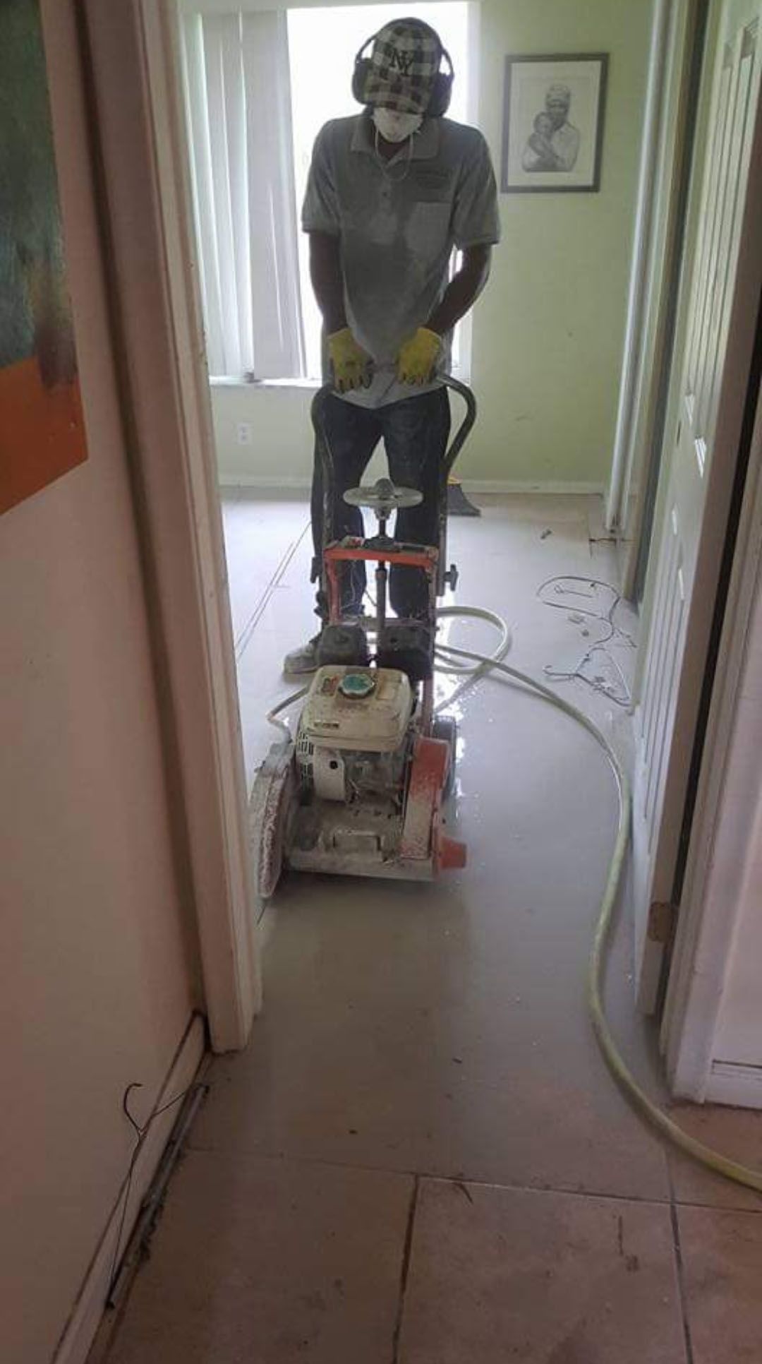 Person operating a floor grinder in a room. Dusty environment, safety gear worn, work in progress.