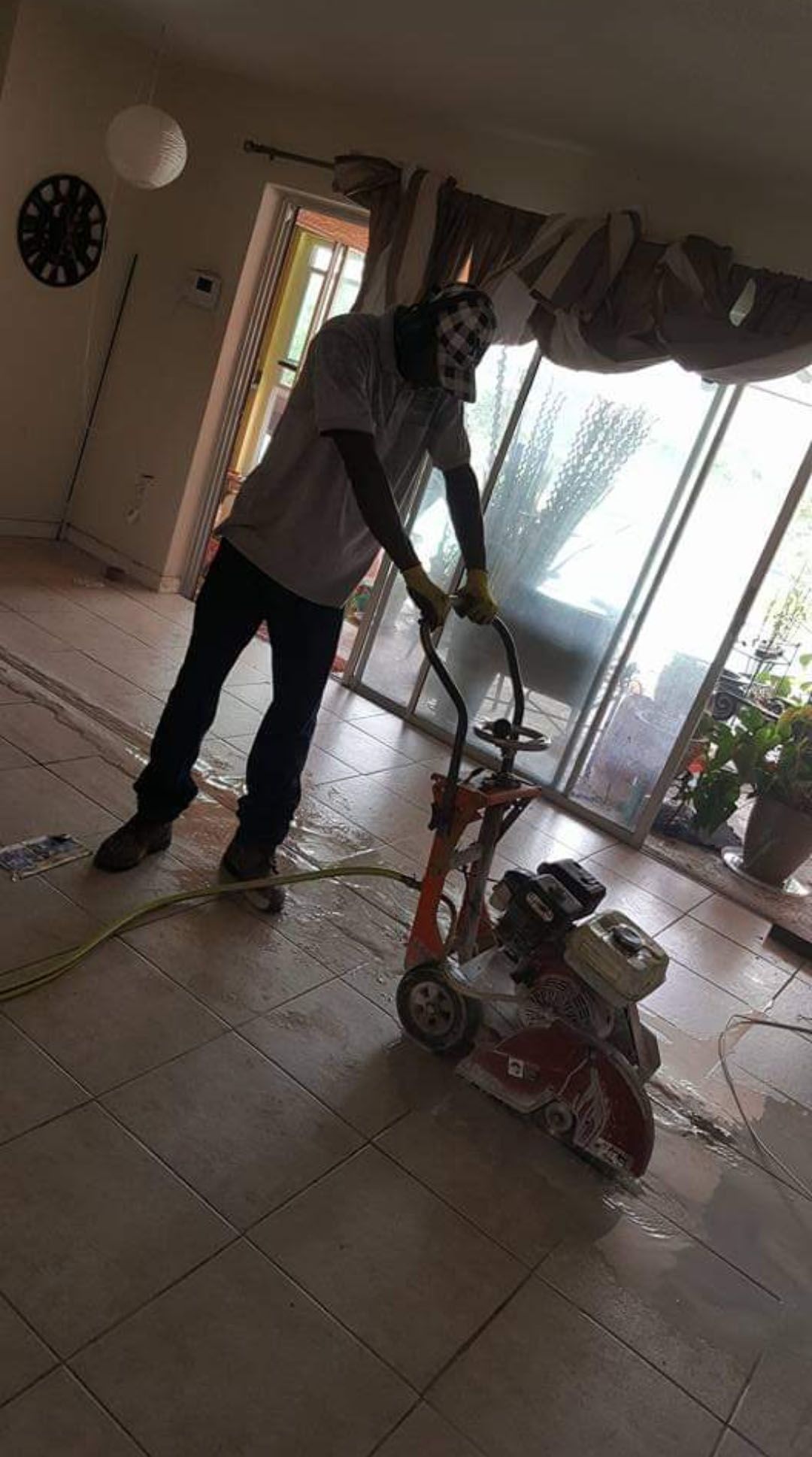 Person using floor saw indoors, next to sliding glass door.