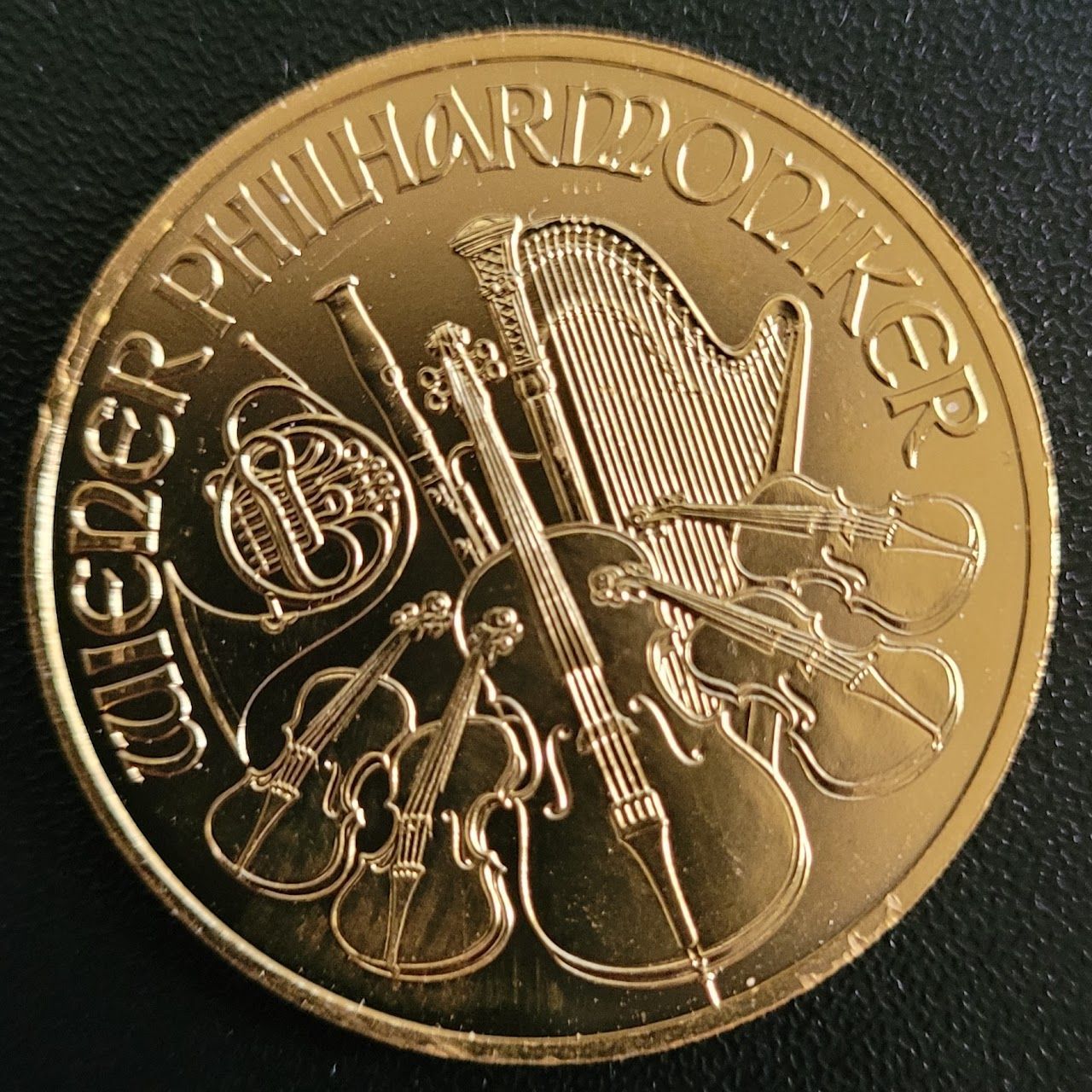 Gold coin with musical instruments: harp, violins, cello, horn. Text: 