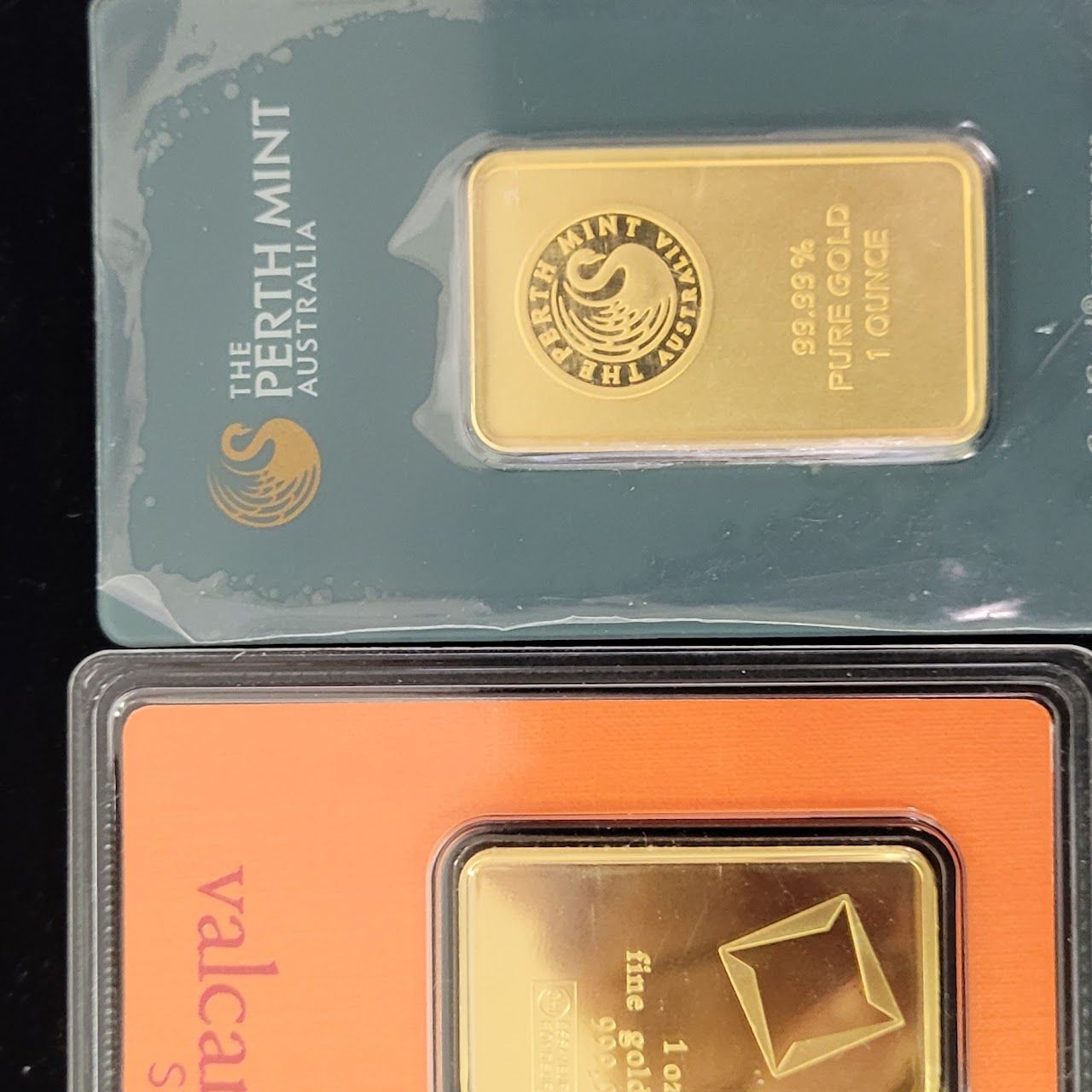 Two gold bars in protective packaging. One is from Perth Mint Australia, the other Valcambi.