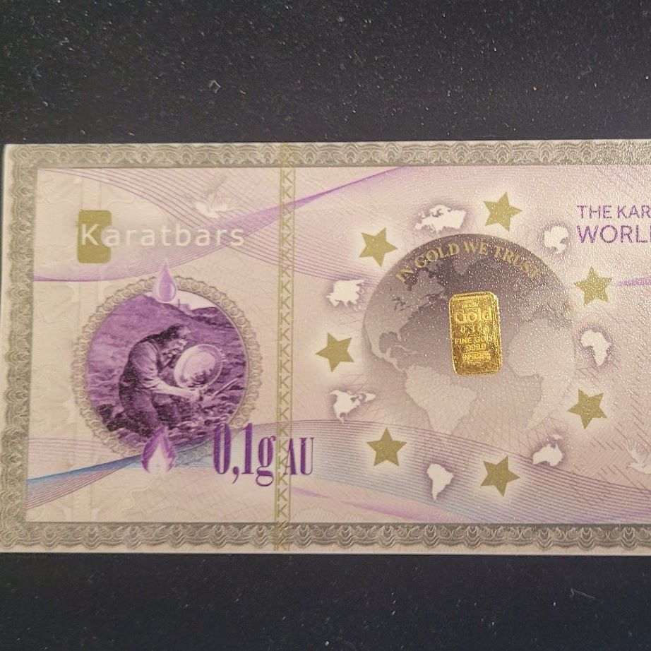 A 0.1g gold bar embedded in a Karatbars certificate. Features a miner illustration and a globe with stars.