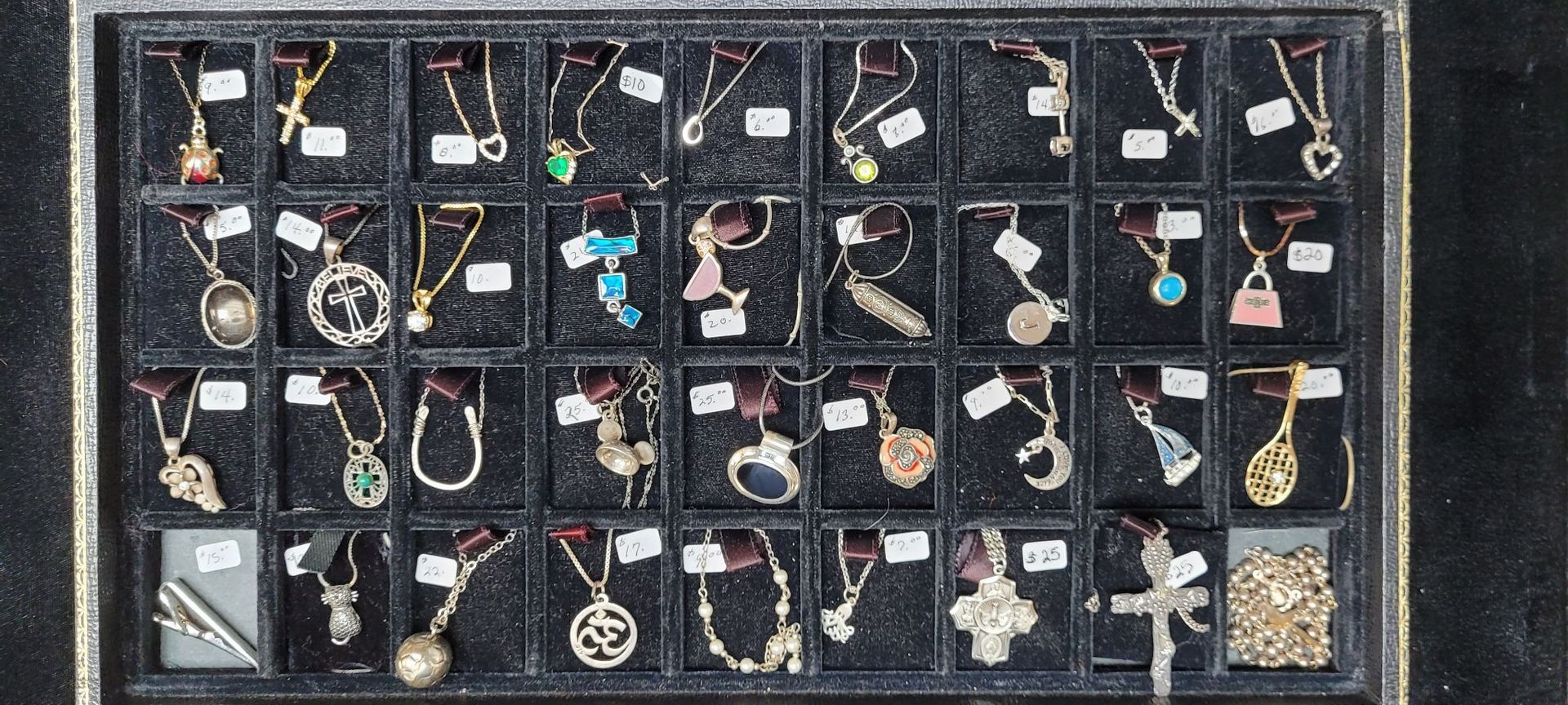 Tray of necklaces with various pendants, displayed in individual compartments.