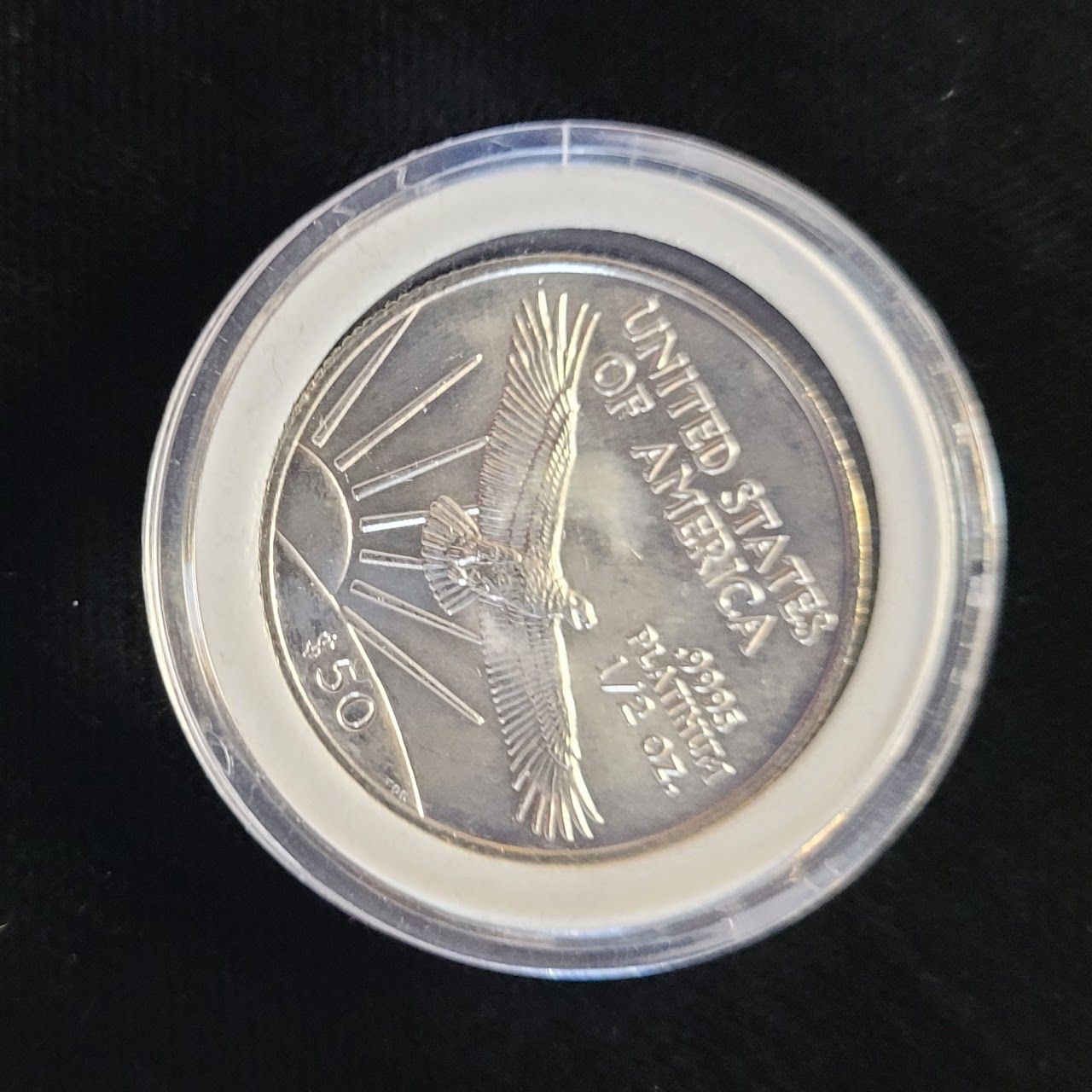 A platinum $50 coin with an eagle design inside a clear protective case.