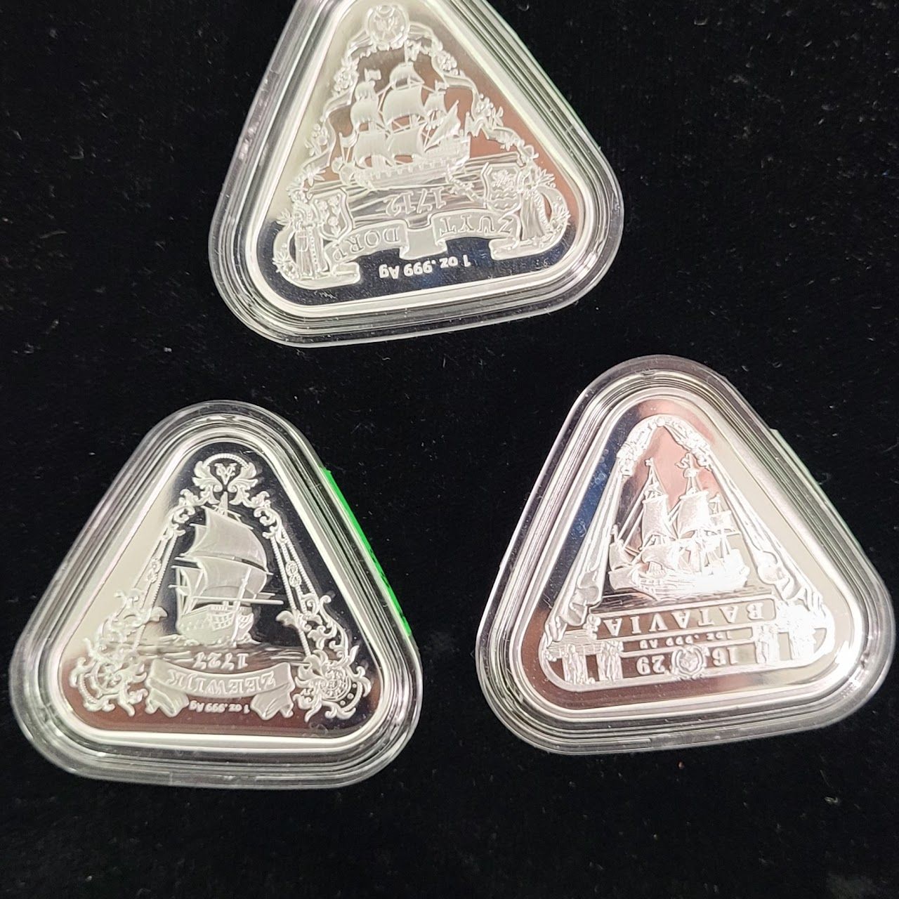 Three silver, triangular coins in clear cases, each with a ship design engraved.